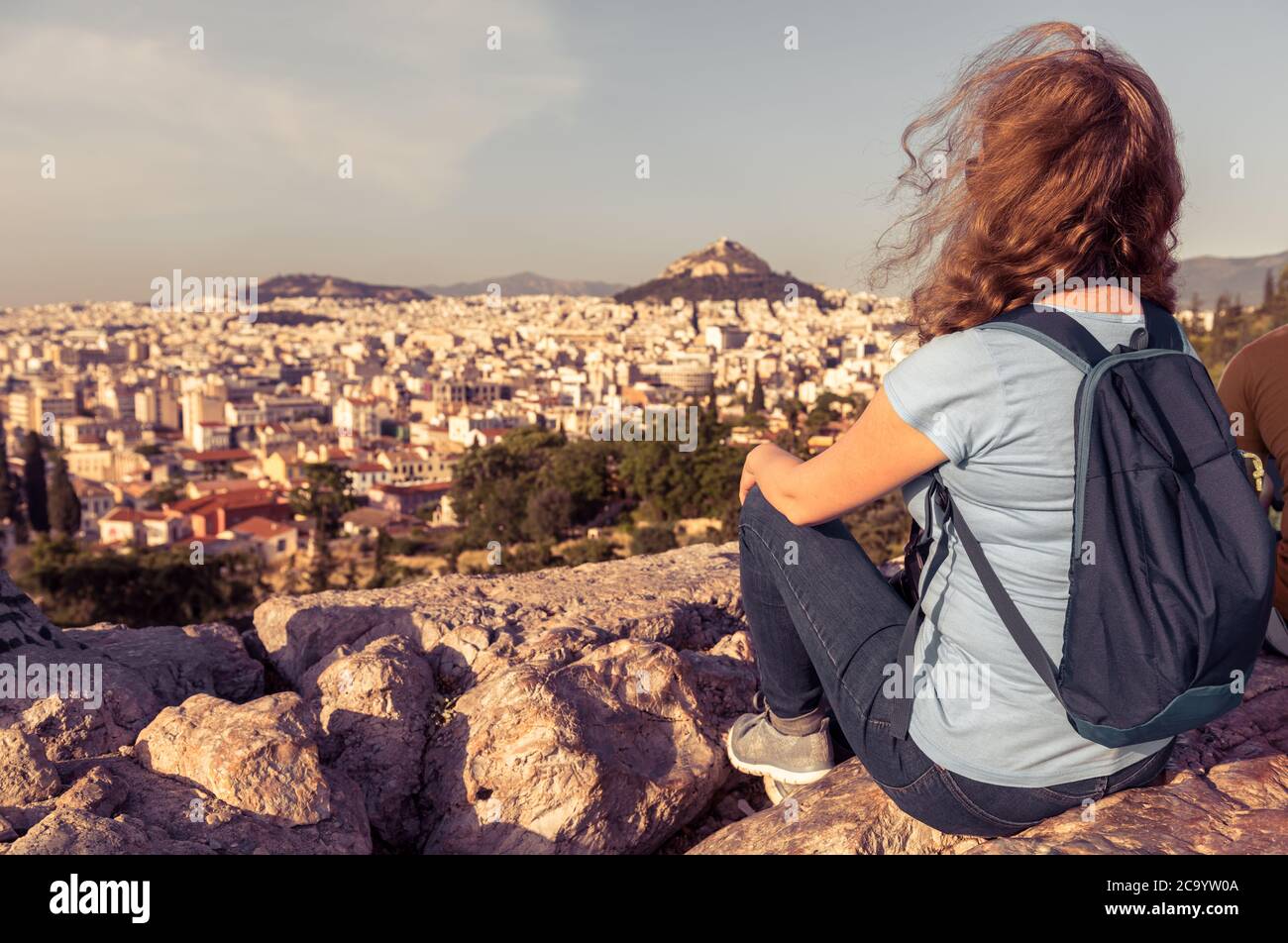 Young person on background of urban landscape of Athens, Greece, Europe. Adult pretty girl tourist relaxes on hilltop overlooking Athens city in summe Stock Photo