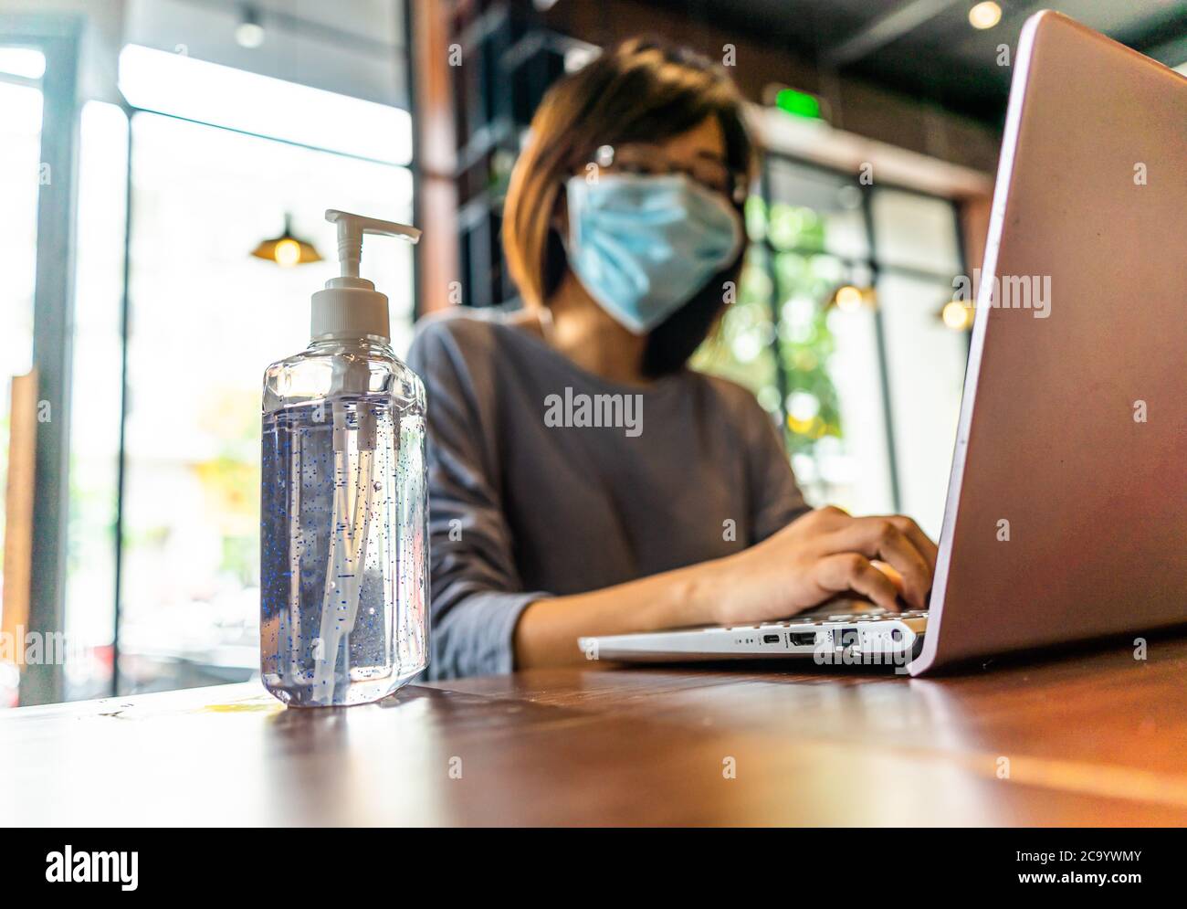Young asian woman using laptop computer working at home with alcohol gel in quarantine for coronavirus wearing protective mask with social distancing Stock Photo