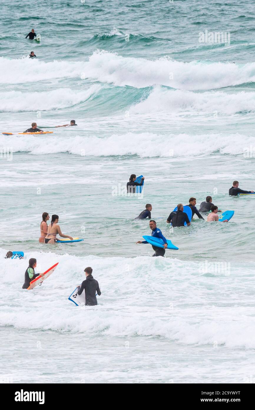 Holidaymakers surfing and bodyboarding in the sea at Fistral in Newquay