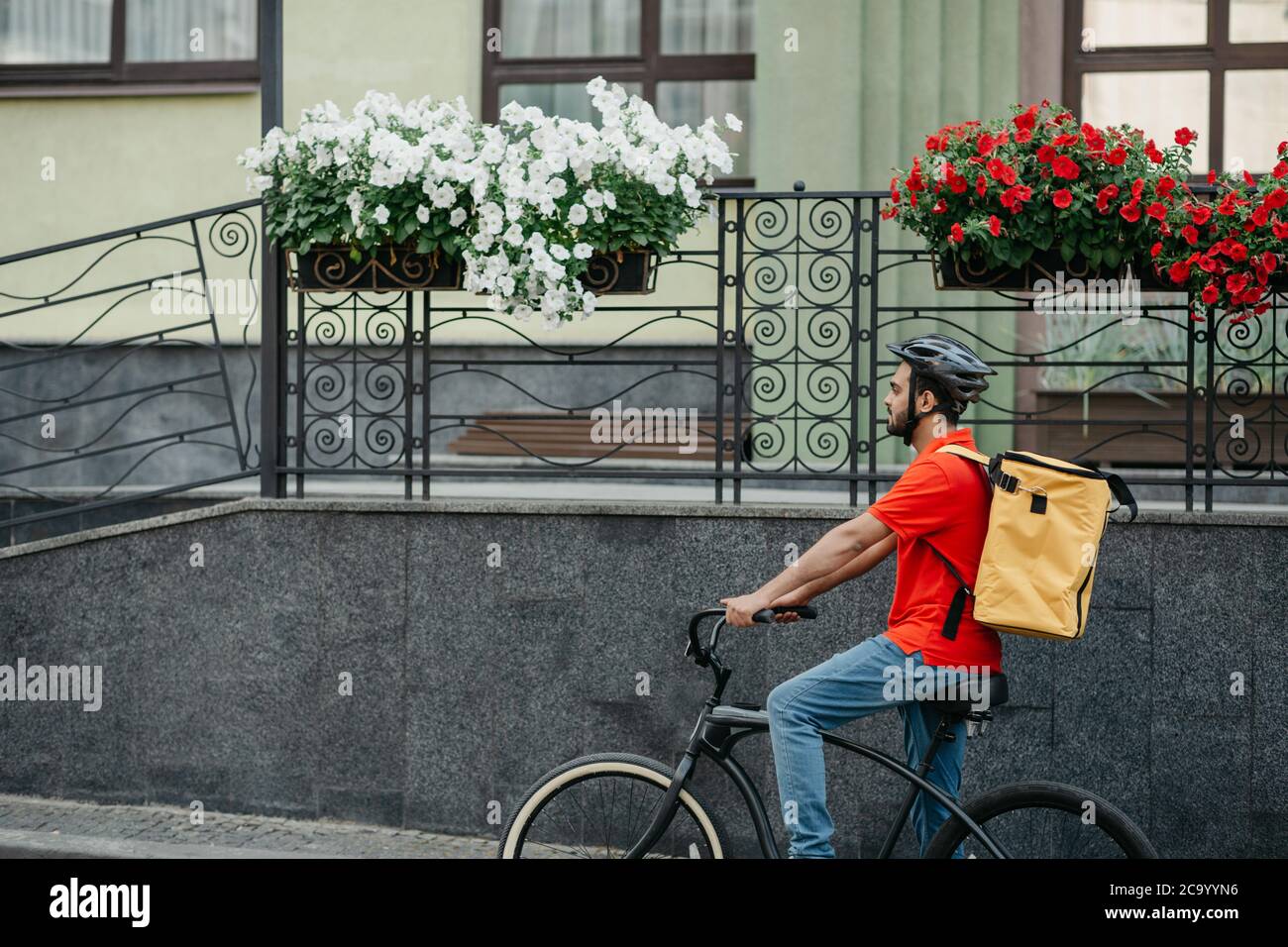 Courier carry out orders for delivery of goods. Man in helmet and big yellow backpack rides bicycle Stock Photo