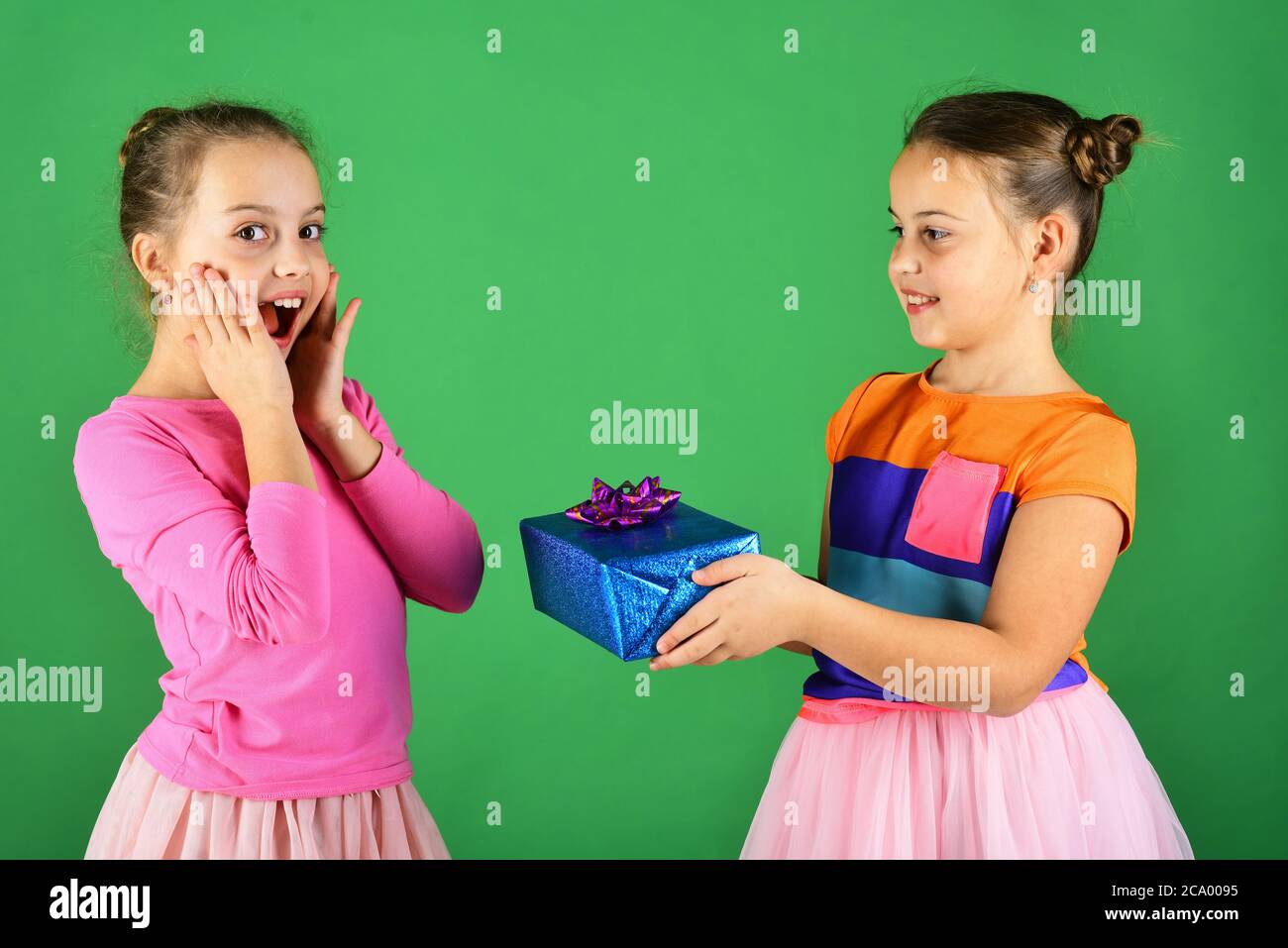 New Year presents concept. Children with shocked faces pose with presents on green background. Sisters with wrapped gift boxes share presents for holiday. Girls open gifts for Christmas. Stock Photo