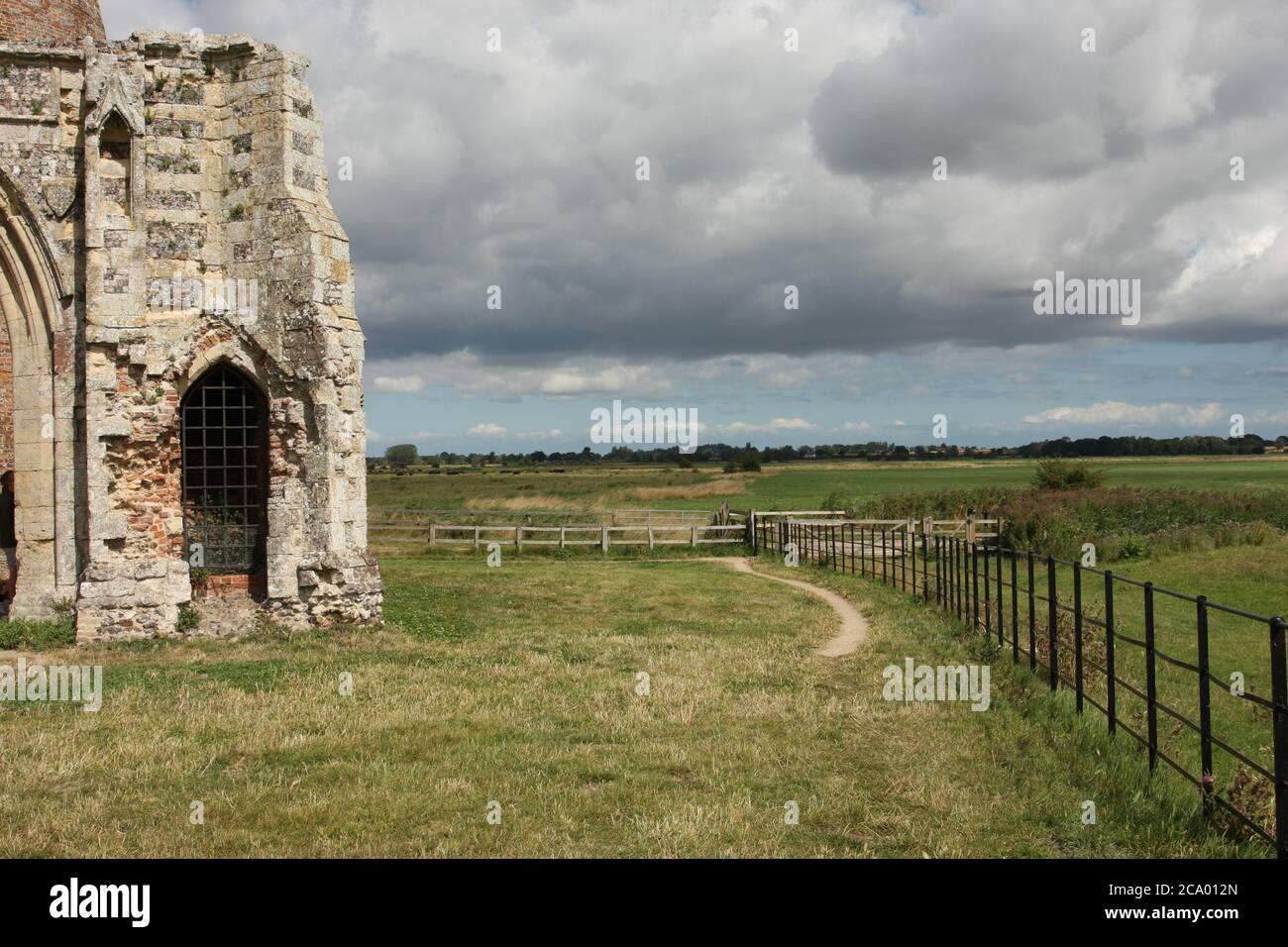 Green flat landscape, dark clouds with ruin of St Benedict's Abbey on left, Norfolk, England Stock Photo