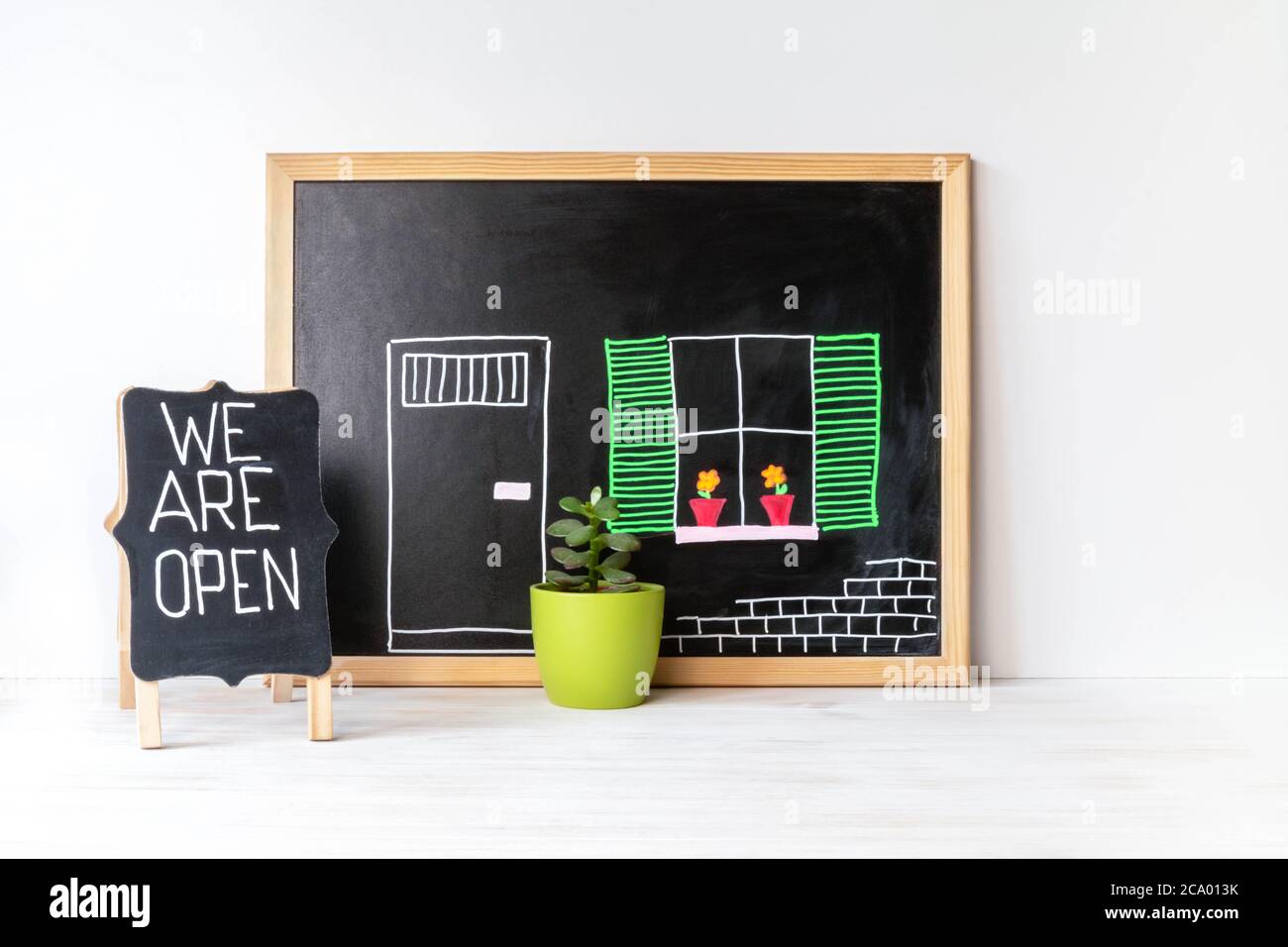 House drawing on blackboard, plant in pot and WE ARE OPEN word on chalkboard. Open singboard near house, drawn on blackboard. Open small business conc Stock Photo
