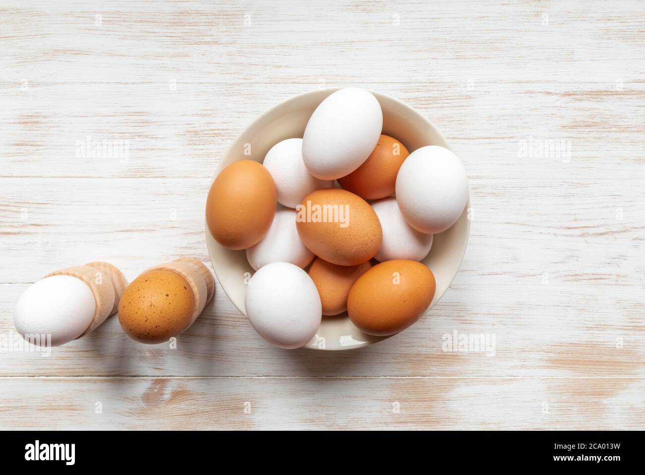 Brown and white eggs in bowl on wood background. Free-range organic eggs. Plate with brown and white chicken eggs, boiled eggs in holders on table Stock Photo