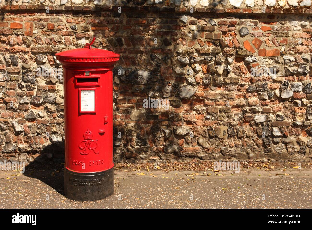 British Royal Mail red post box in front of flint wall Stock Photo