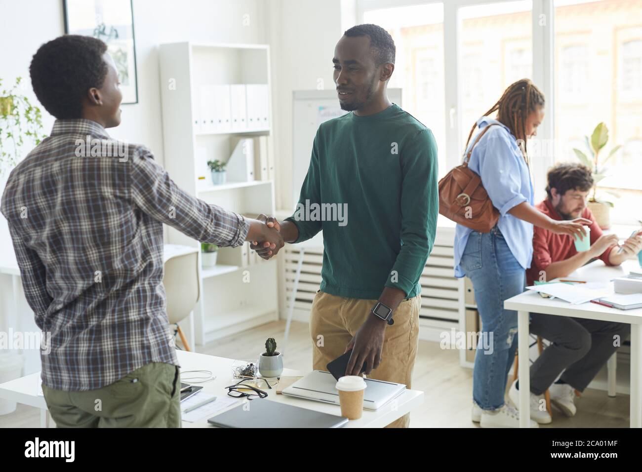 Portrait of young African-American man dressed in casual wear shaking hands with colleague across table during first day at new job, copy space Stock Photo