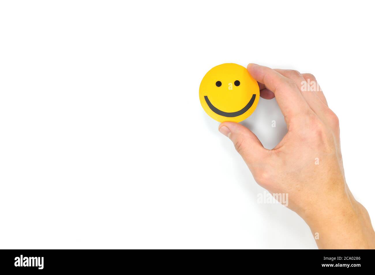 Happiness and be positive concept. Male hand holding yellow smiling face in white background with copy space. Stock Photo