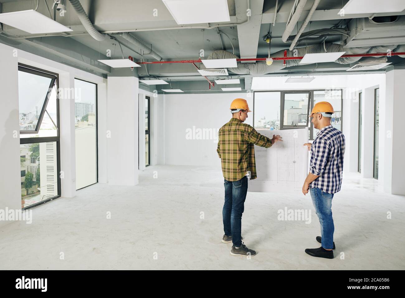 Two young construction engineers discusing blueprint of building and planning works for today Stock Photo