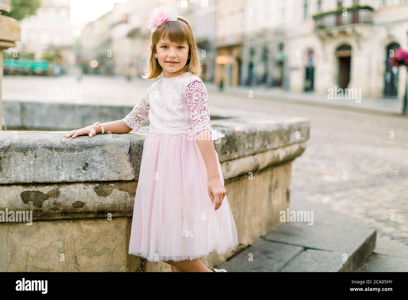 Portrait of a little girl in pink dress and flower accessories in hair ...