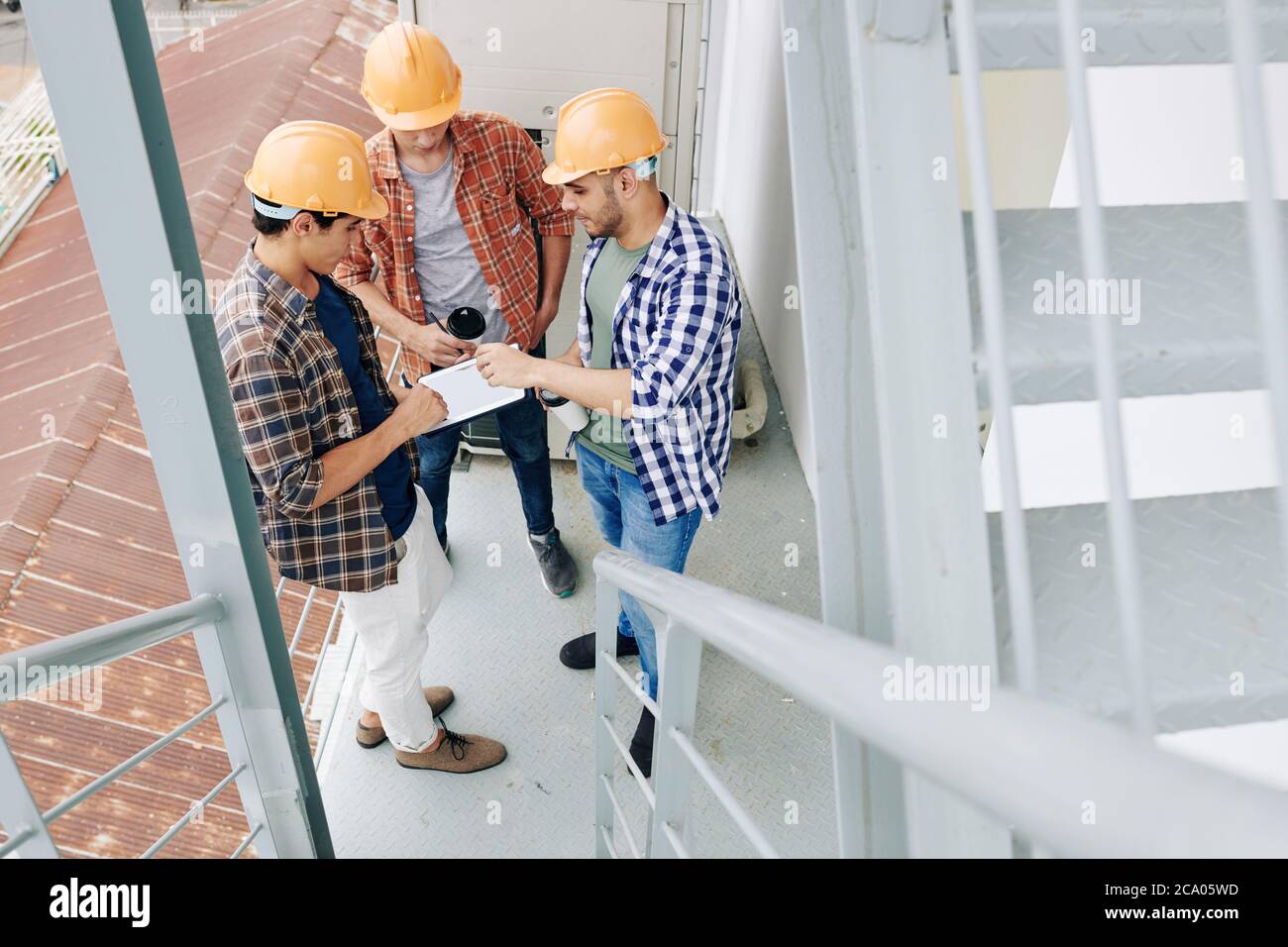Young builders drinking morning cafe and checking plan of works on tablet computer Stock Photo