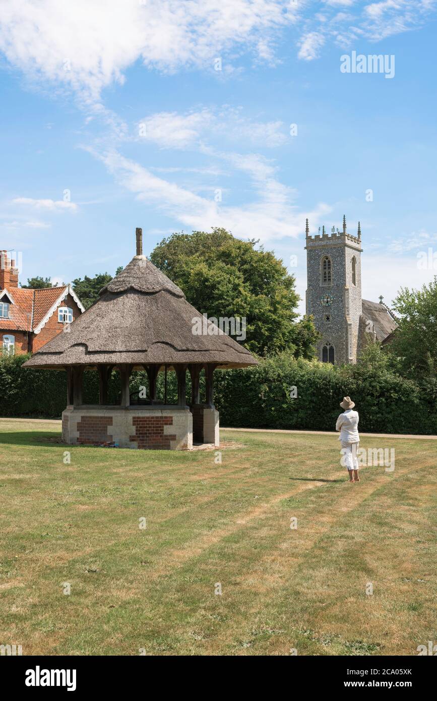 England summer countryside, view of a solo woman traveller standing on a typical English village green and looking at a nearby church, Norfolk UK Stock Photo