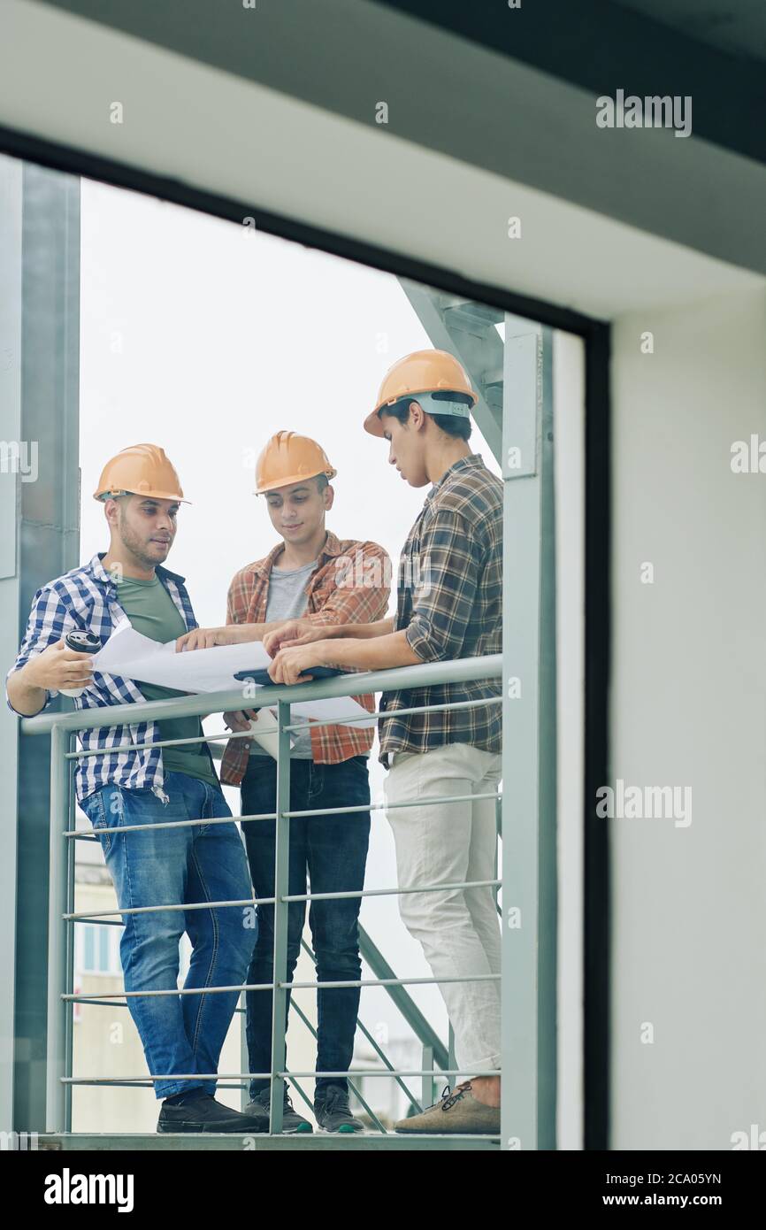 Young builders checking building blueprint before starting starting construction works in house Stock Photo