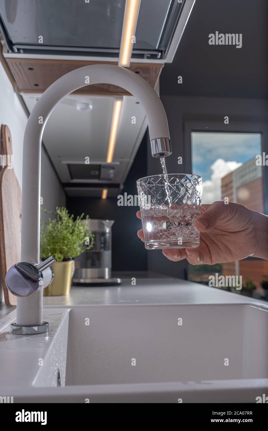 hand holding a glass of water. a man pouring water from filter tap. Stock Photo