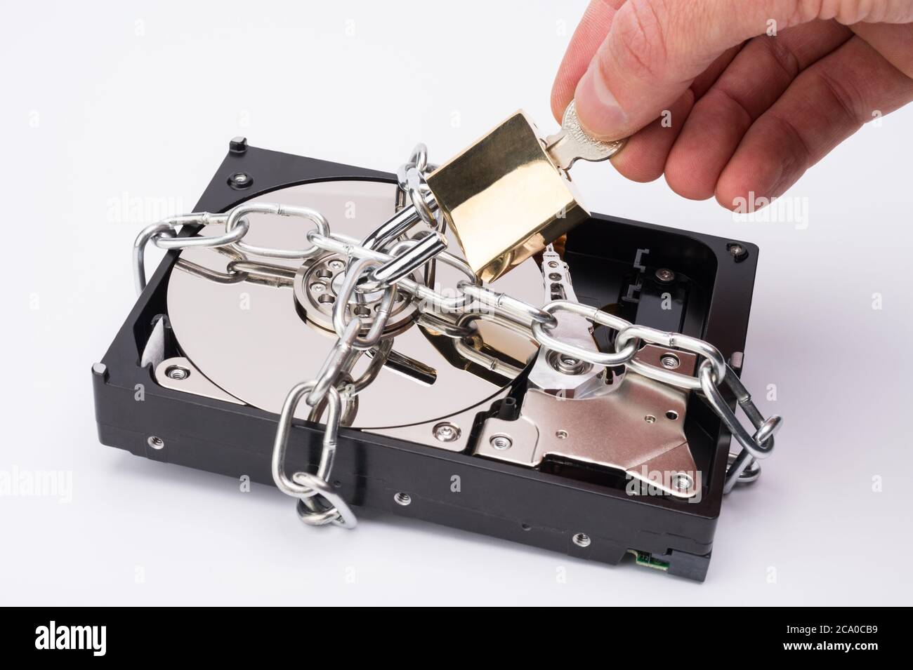 A 3.5' hard disk drive (HDD) secured by a chain with a man's hand unlocking the padlock. Stock Photo