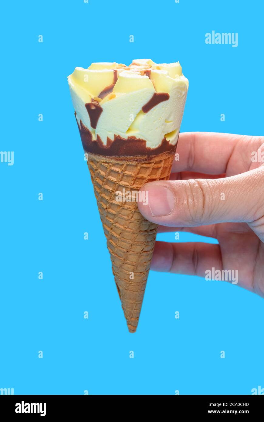 hand holding a fresh vanilla flavor ice cream cone on blue background ...