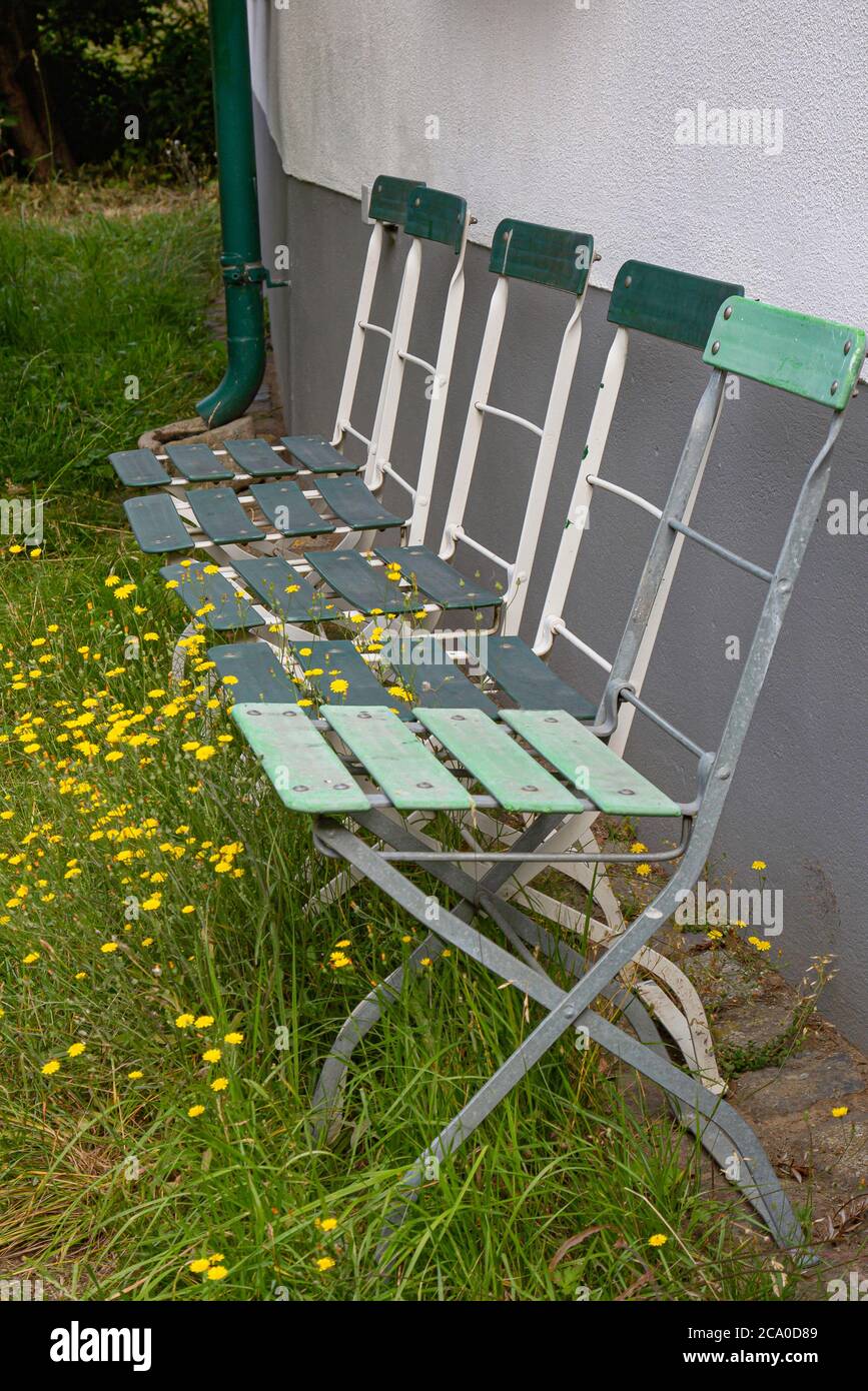 Four old green faded garden chairs in front of a wall with grass and