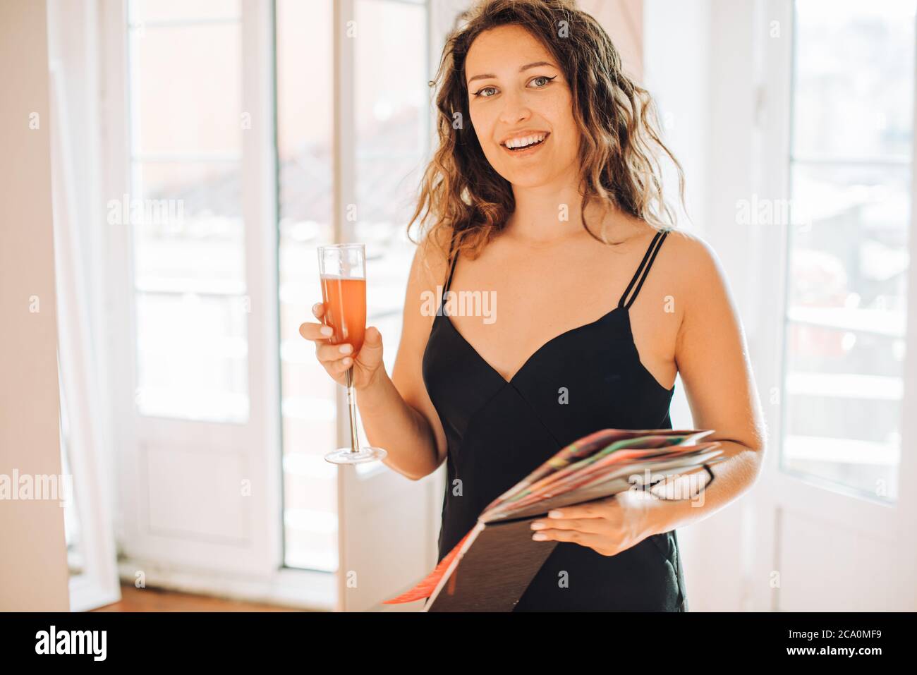 Woman in black dress holding glass of wine and album looking at camera Stock Photo