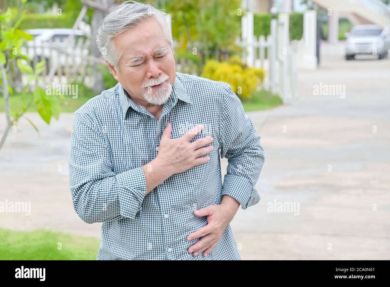 Senior asian man having painful chest heart attack at outdoors home park - heart disease concept Stock Photo