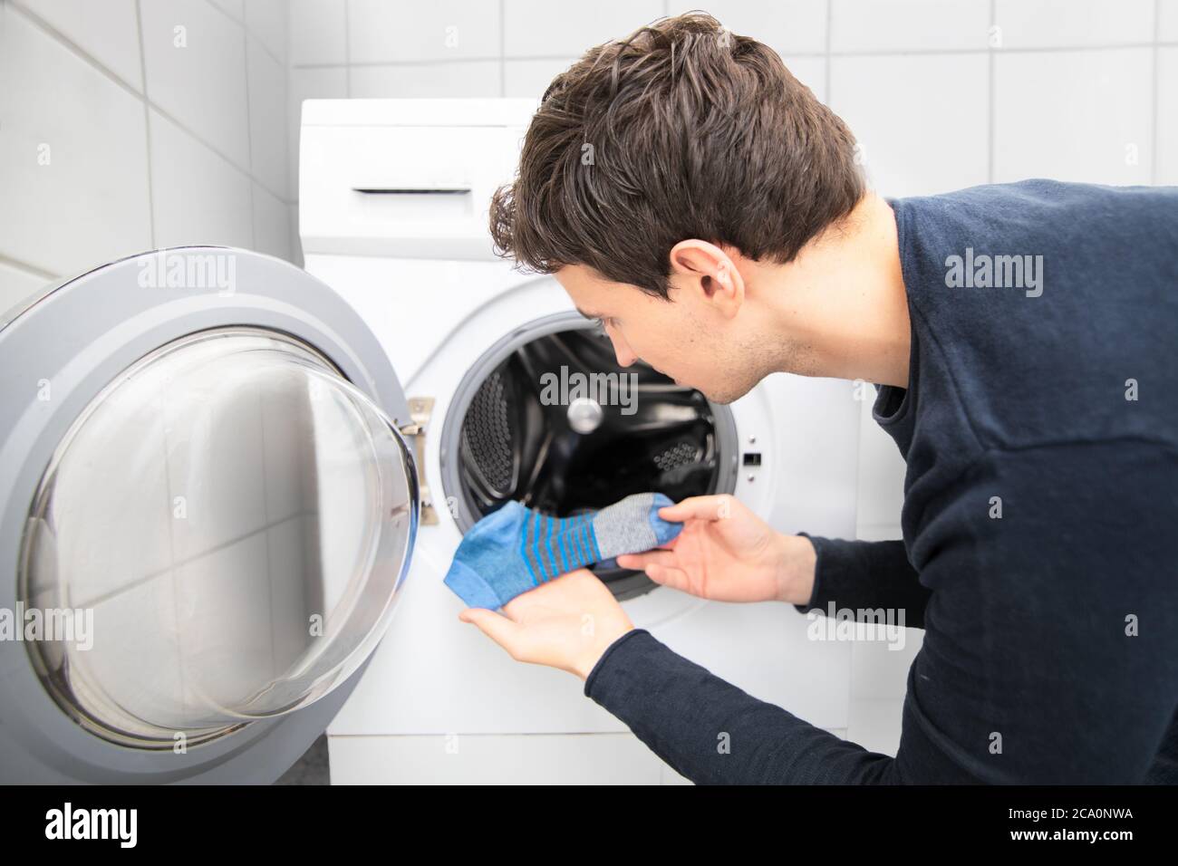 man looking for missing socks in washing mashine and found only one blue sock Stock Photo