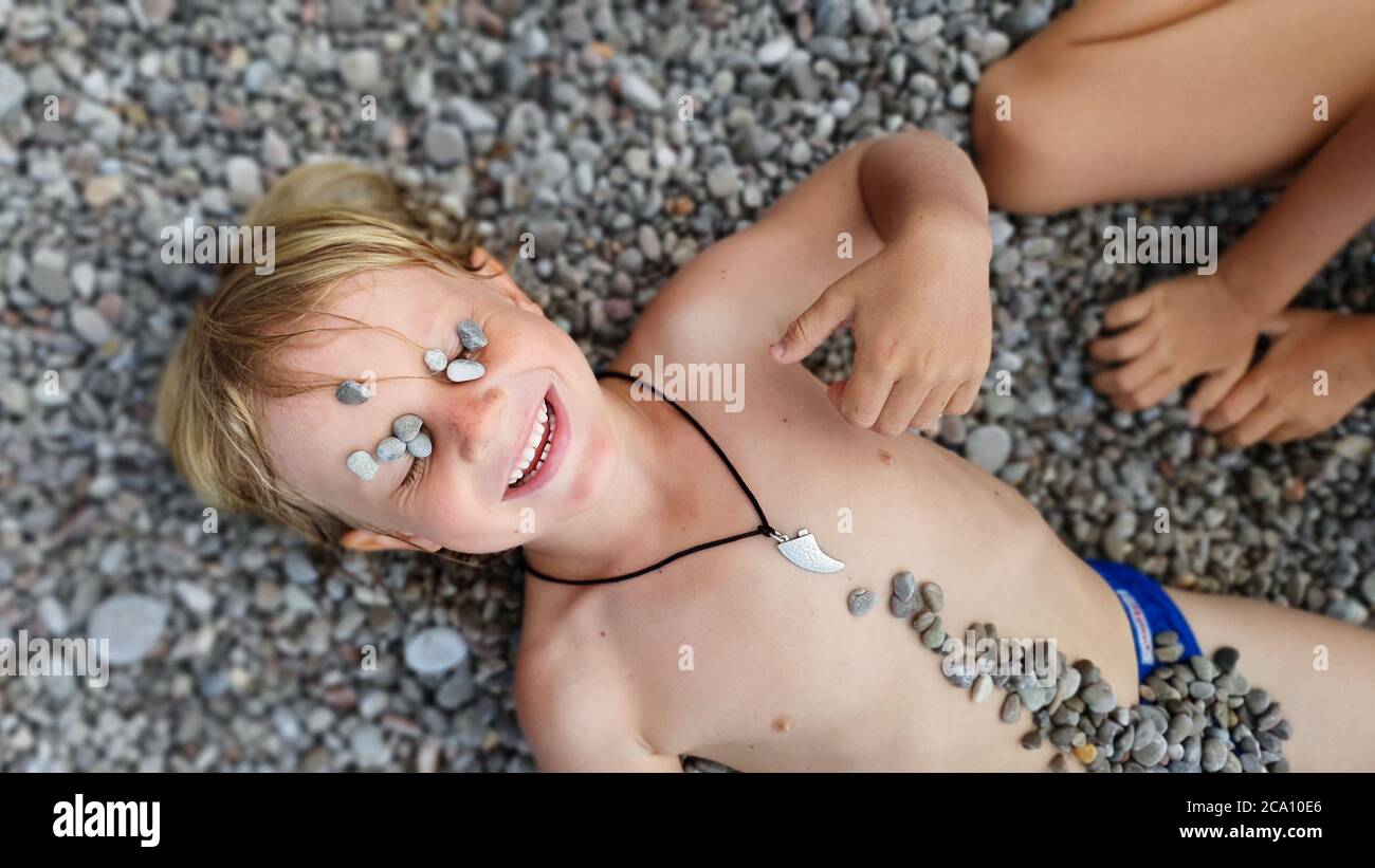 On sunny beach happy kids have fun, lying down on hot pebble, sunbathing, warming after swimming in sea. Active children lifestyle, summer vacation Stock Photo