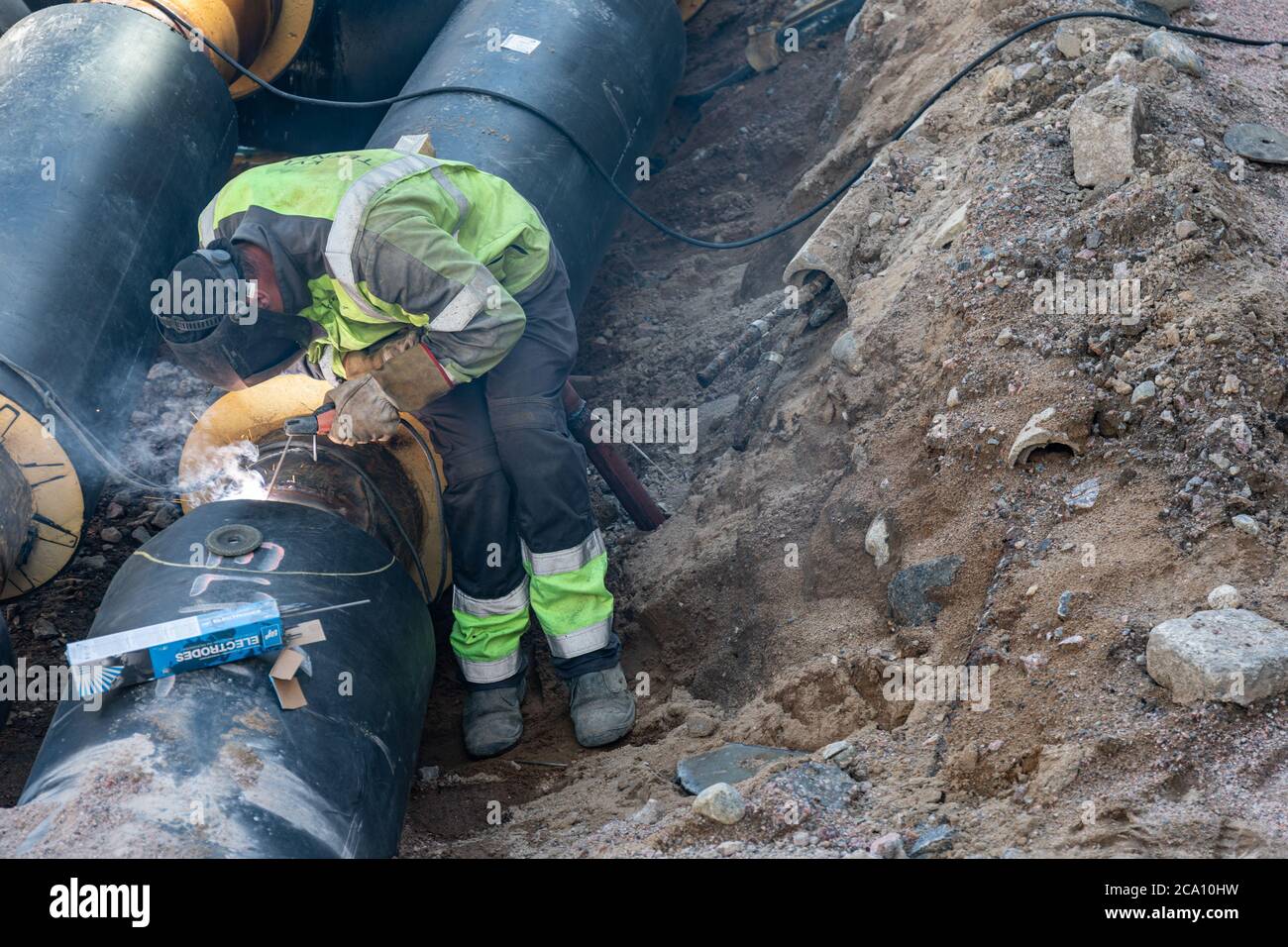 Welder worker electric welding joint on insulated district heating pipe in Helsinki, Finland Stock Photo