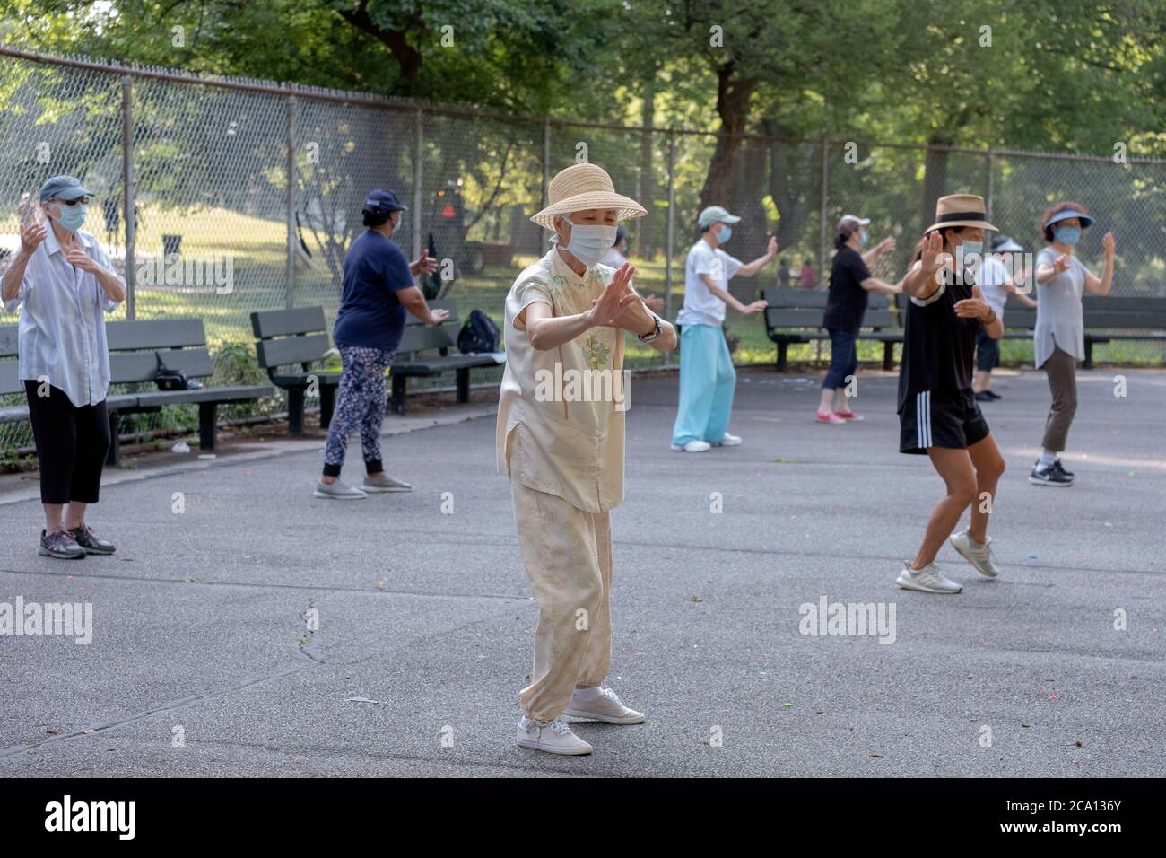 Men & women of various ages and ethnicities attend a morning Tai Chi class wearing surgical masks and social distancing. in Queens, New York City. Stock Photo