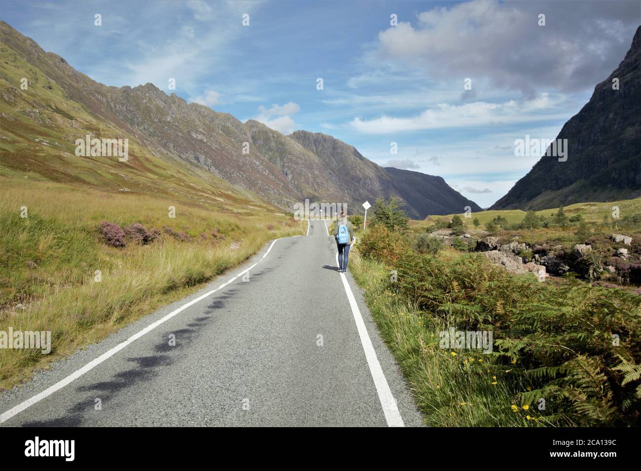 A young girl walking along the road with her backpack in Glencoe in Scottish Highlands in Summer, Scotland, Great Britain Stock Photo