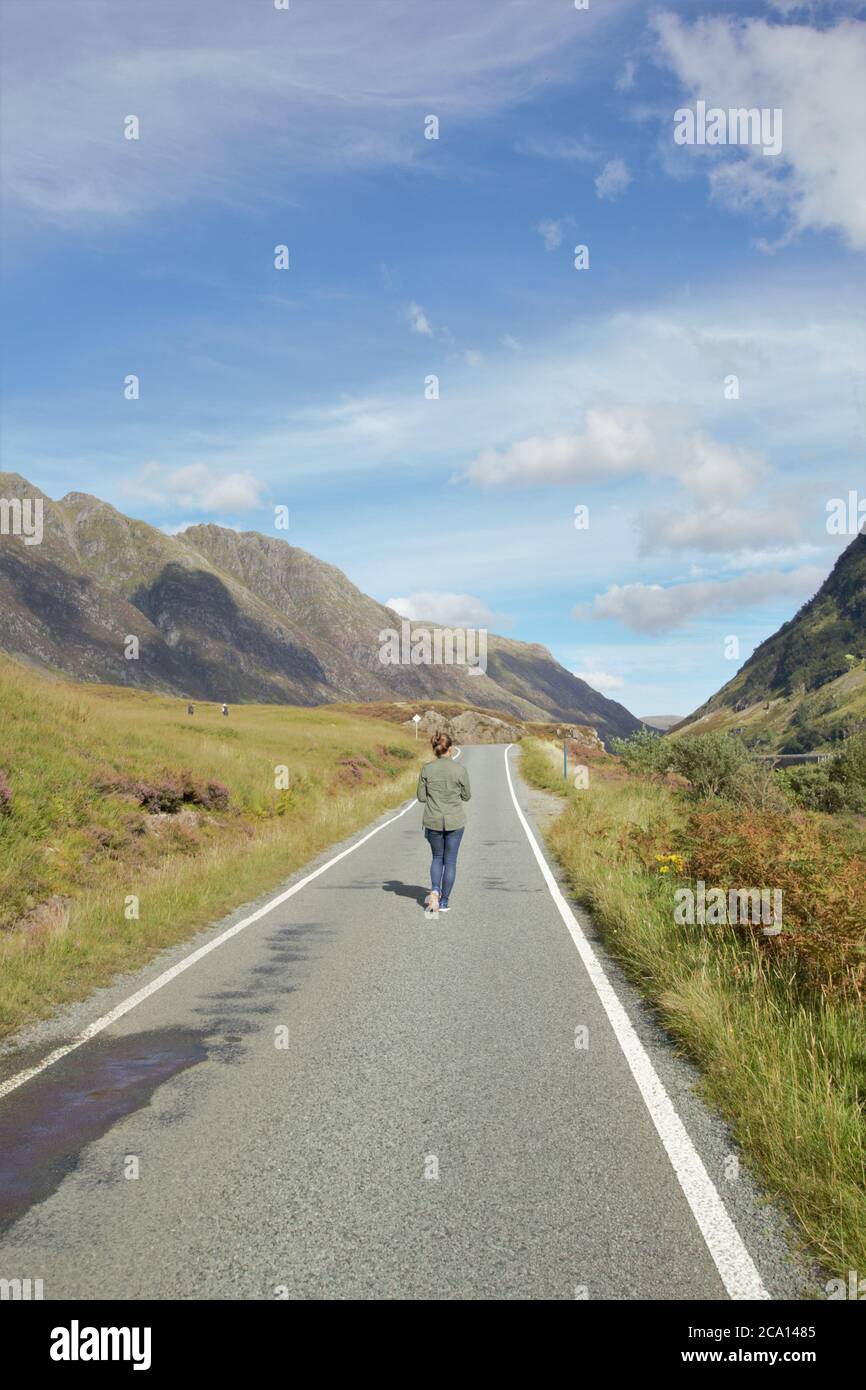 A young girl walking along the road with her backpack in Glencoe in Scottish Highlands in Summer, Scotland, Great Britain Stock Photo