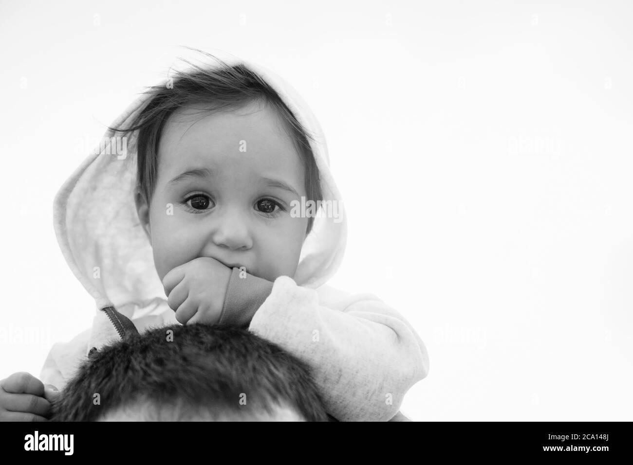 Close up of small baby girl in hood sitting on father's shoulders on the sky background Stock Photo