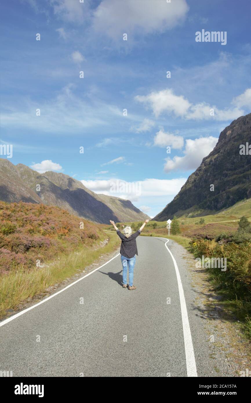 A woman walking along the road in Glencoe in Scottish Highlands in Summer, Scotland, Great Britain Stock Photo