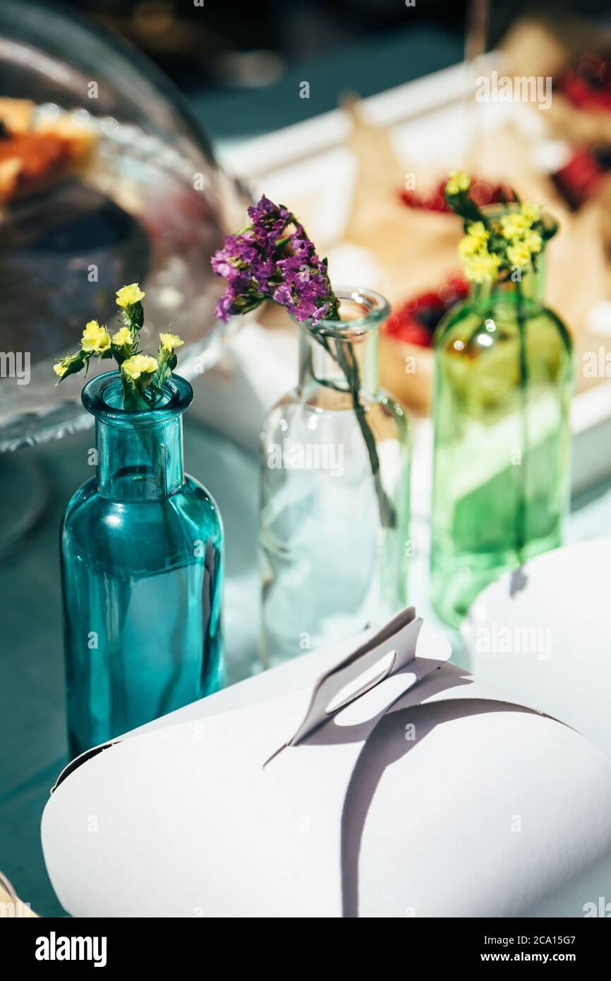 Fresh little multicolored statice salem or limonium sinuatum flowers in blue, white and green bottles outdoors. A decoration of the table Stock Photo