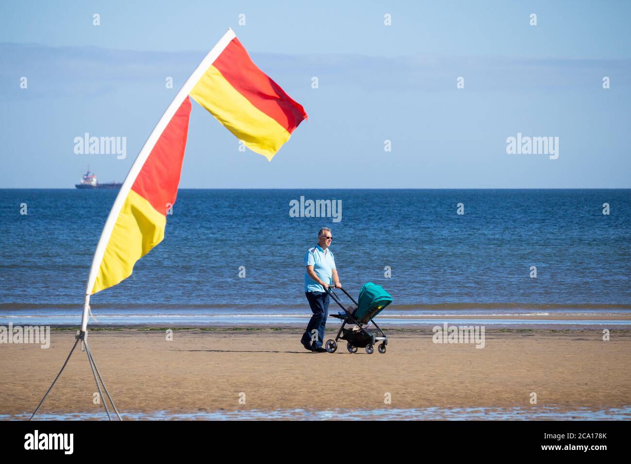 Elderly man/grandparent pushing pram on beach. UK Stock Photo