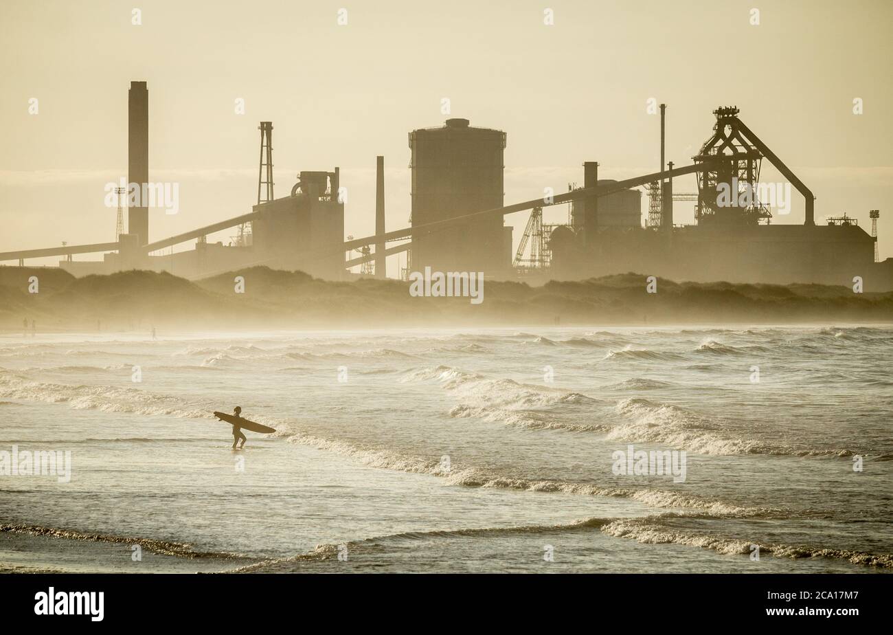 Surfers heading out from Redcar beach with Redcar steelworks in background. Stock Photo