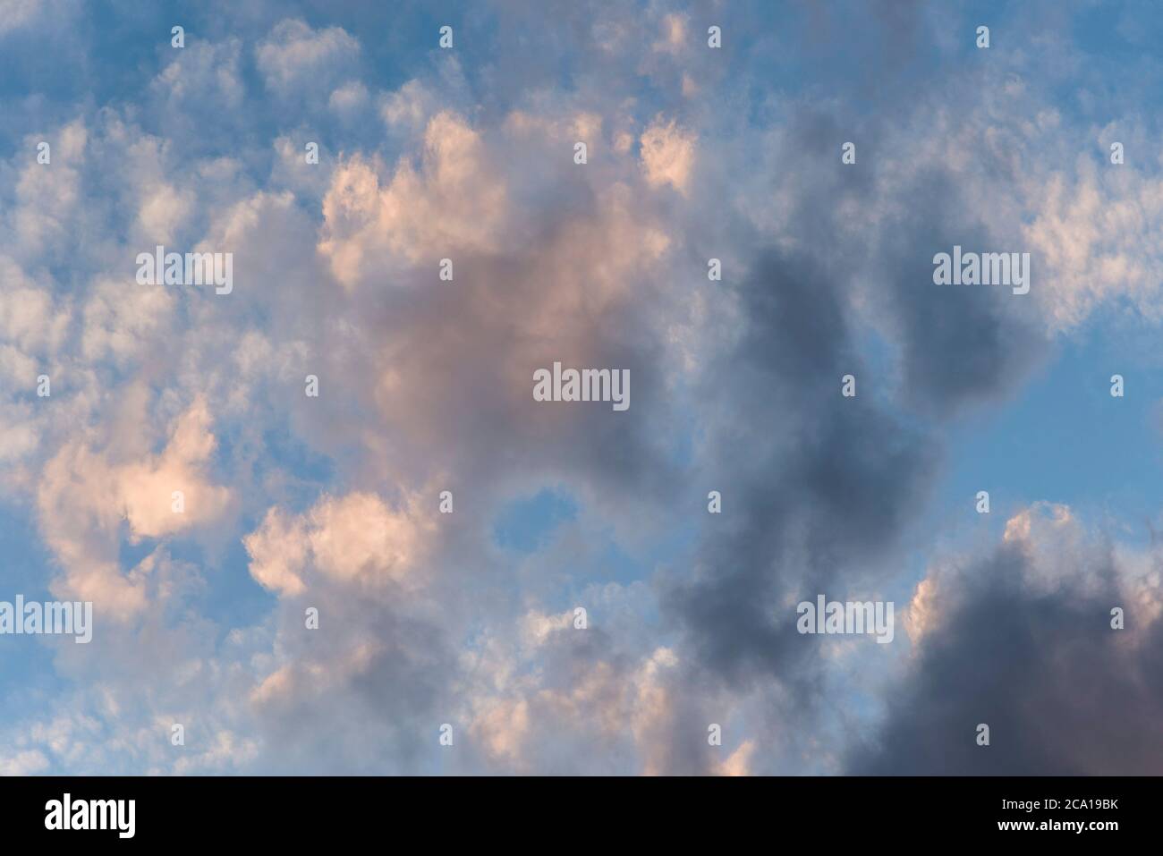 Cloudscape: cloudy sky, grey and white clouds illuminated by the evening sun over a bright blue sky Stock Photo