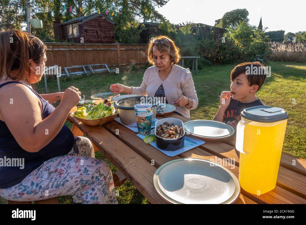A family eat a meal together on a trestle table outside in the back garden. Stock Photo
