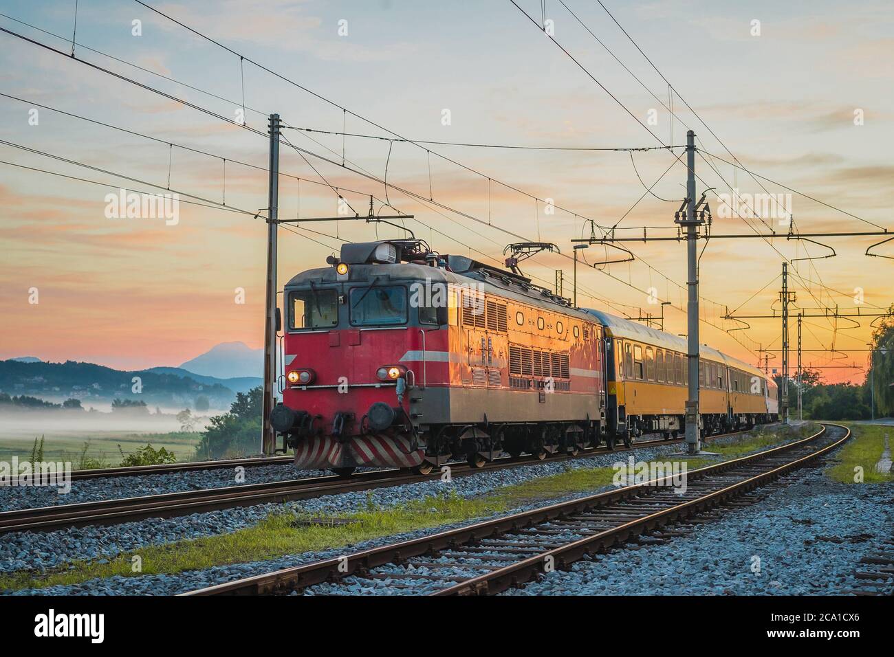 Night passenger train from Prague to Rijeka on its way over the Ljubljana marshes in early romantic morning with sunrise. Fast overnight express to Da Stock Photo