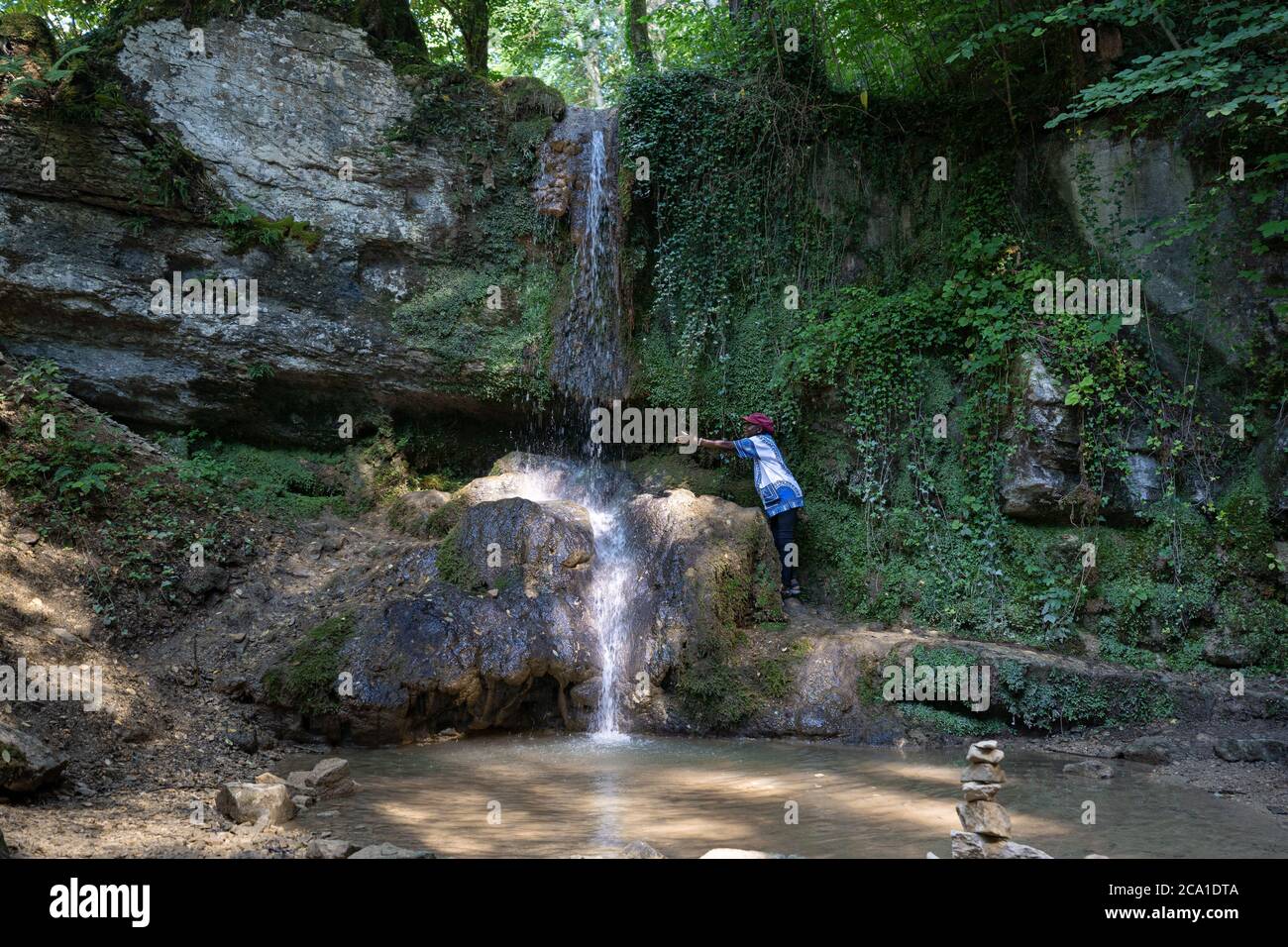 African woman reach out to the water of a waterfall at a hot day in summer. Linner waterfall is the biggest waterfall in canton of Aargau, located at Stock Photo