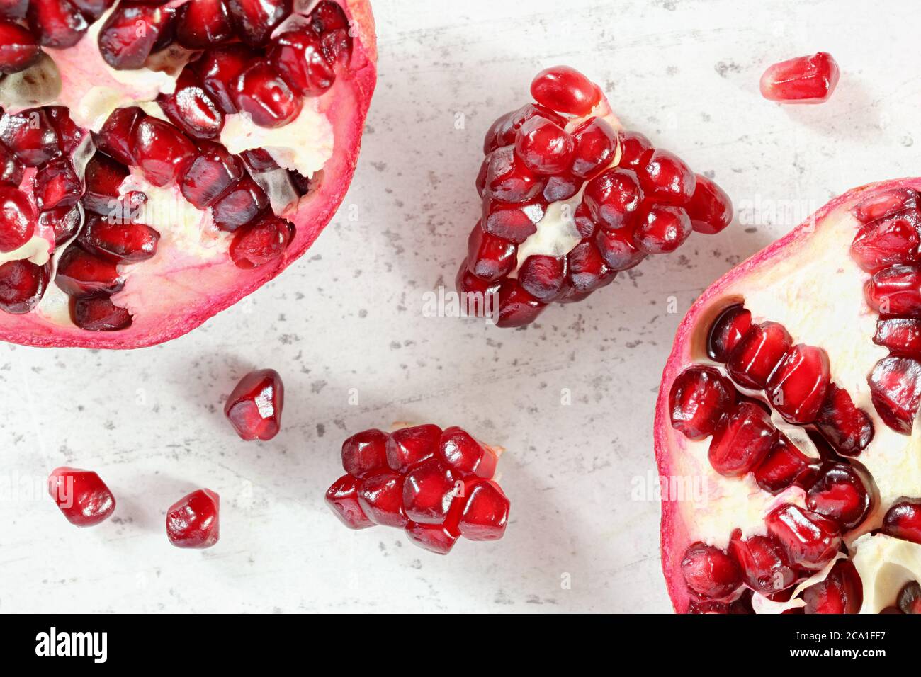 Tabletop closeup view - pomegranate half, clusters of gem like fruits scattered on white board. Stock Photo