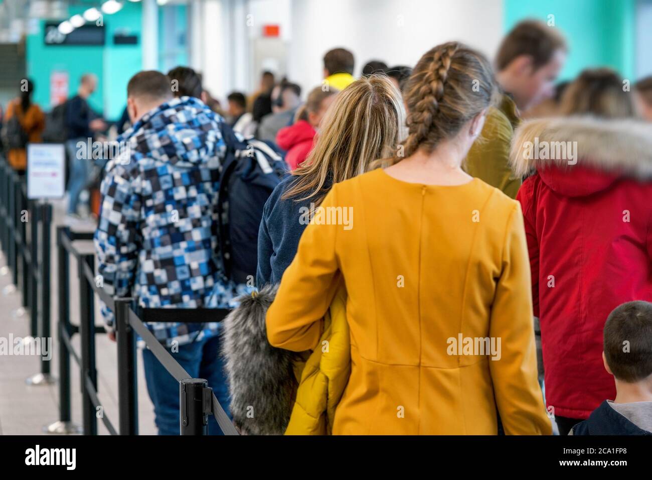 Group of anonymous people waiting at airport gate line to board an airplane, queue crowd seen from behind. Stock Photo