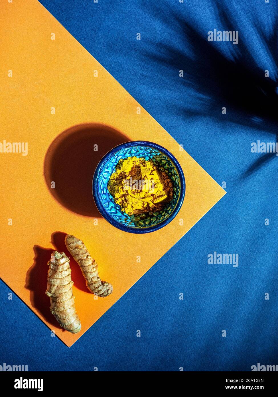 Turmeric (curcumin, Curcuma Longa Linn), powder in blue ceramic bowl and rhizome on orange and blue background. Powerful immunity booster.  Stock Photo