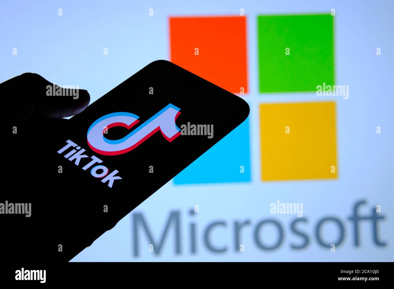 Stone / UK - August 3 2020: TikTok app on the silhouette of mobile hold in hand. Microsoft logo seen on blurred display behind. Selective focus. Real Stock Photo