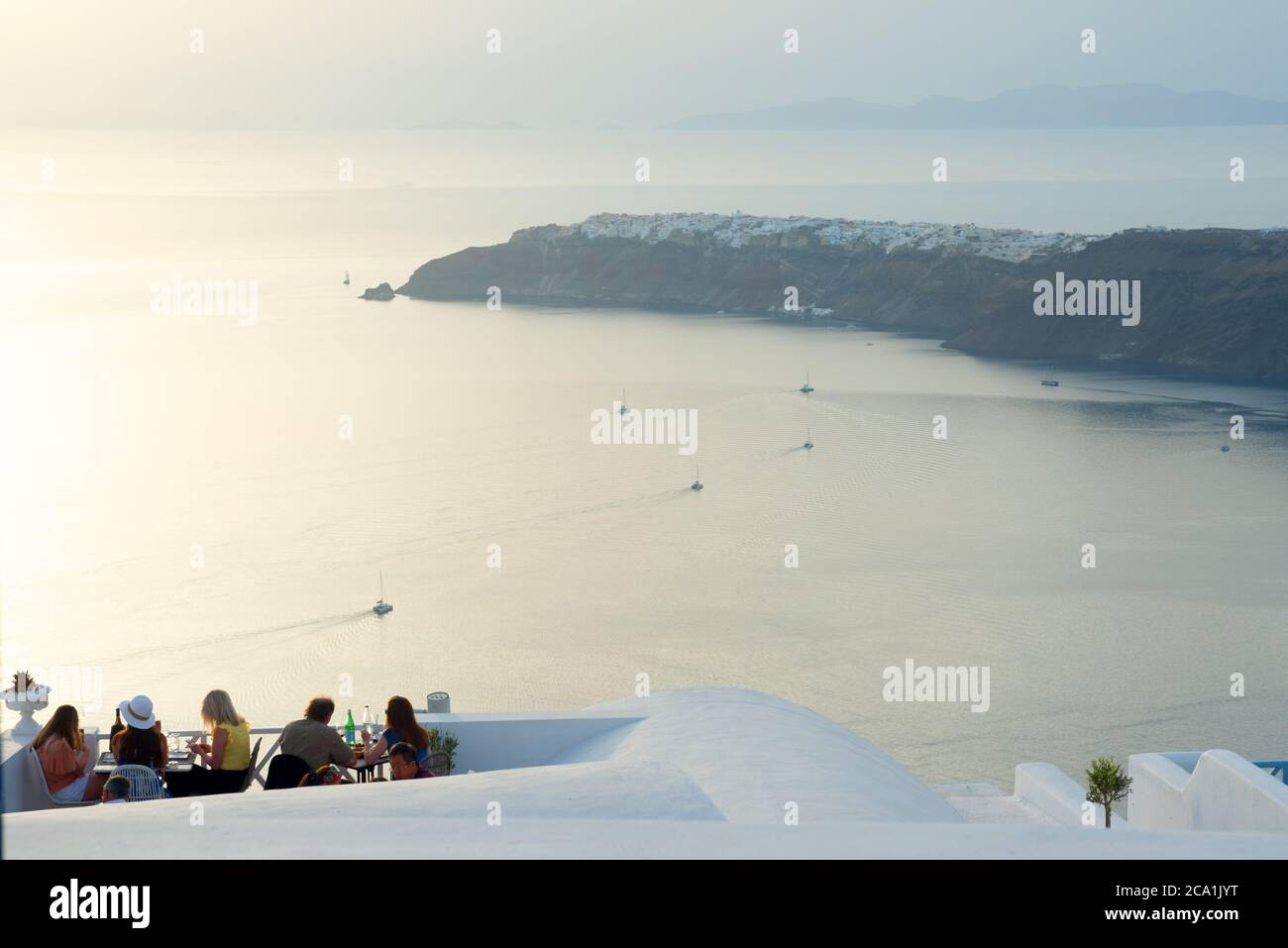 People sitting on a terrace with a scenic view of sea and Oya village on a cliff. Santorini. Greece Stock Photo