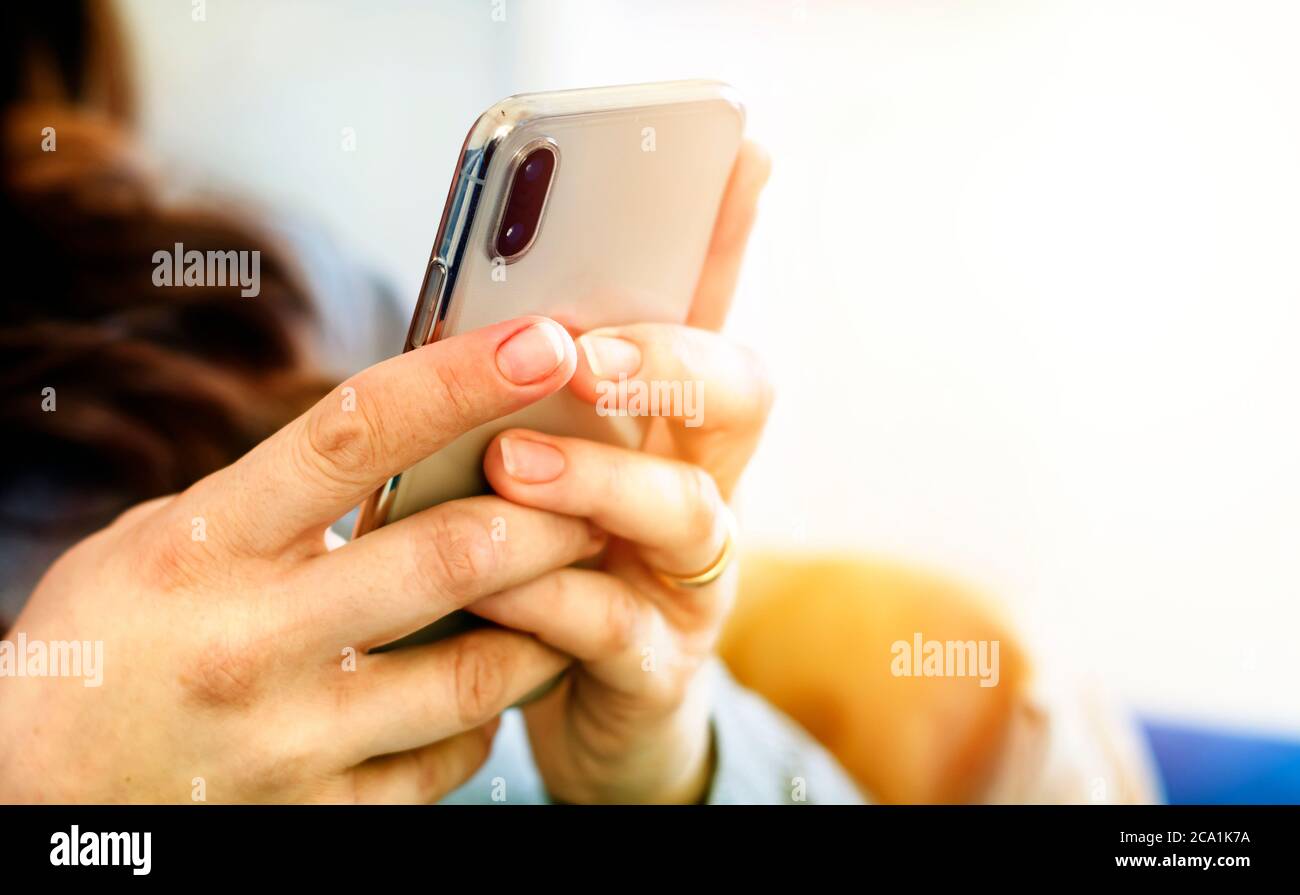 the hands of a young caucasian brunette woman while holding a smartphone typing on the touch screen. Technology and mobile connection. Stock Photo