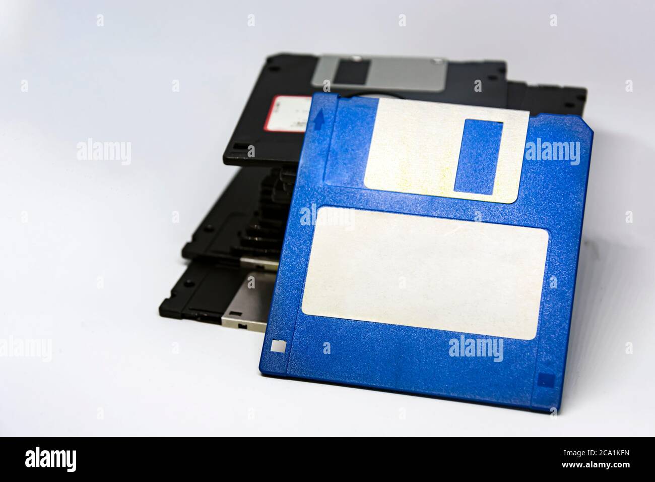 a blue floppy disk with a white sticky label with a bunch of other black floppy disks stacked in the background. Outdated data storage technology. Stock Photo