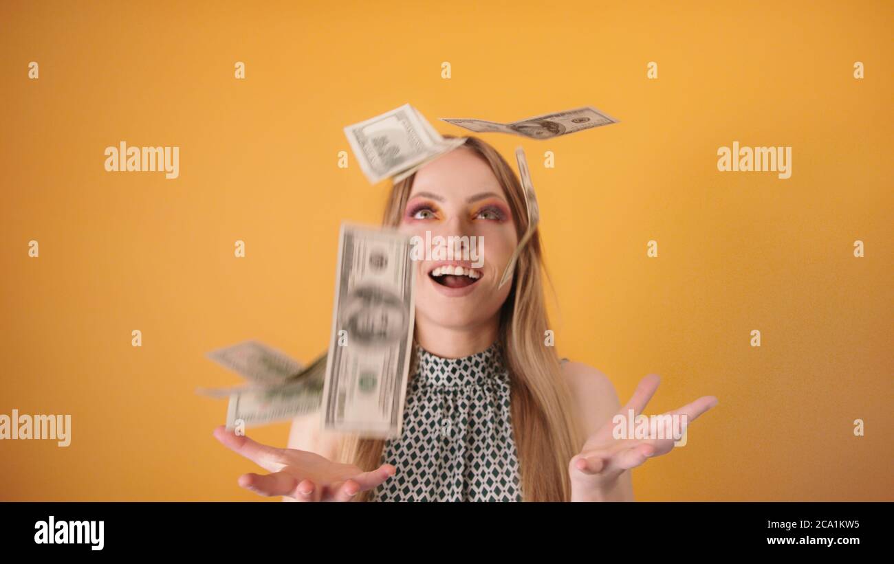 Money rain. Excited beautiful caucasian woman catching the falling money isolated on orange background. High quality photo Stock Photo
