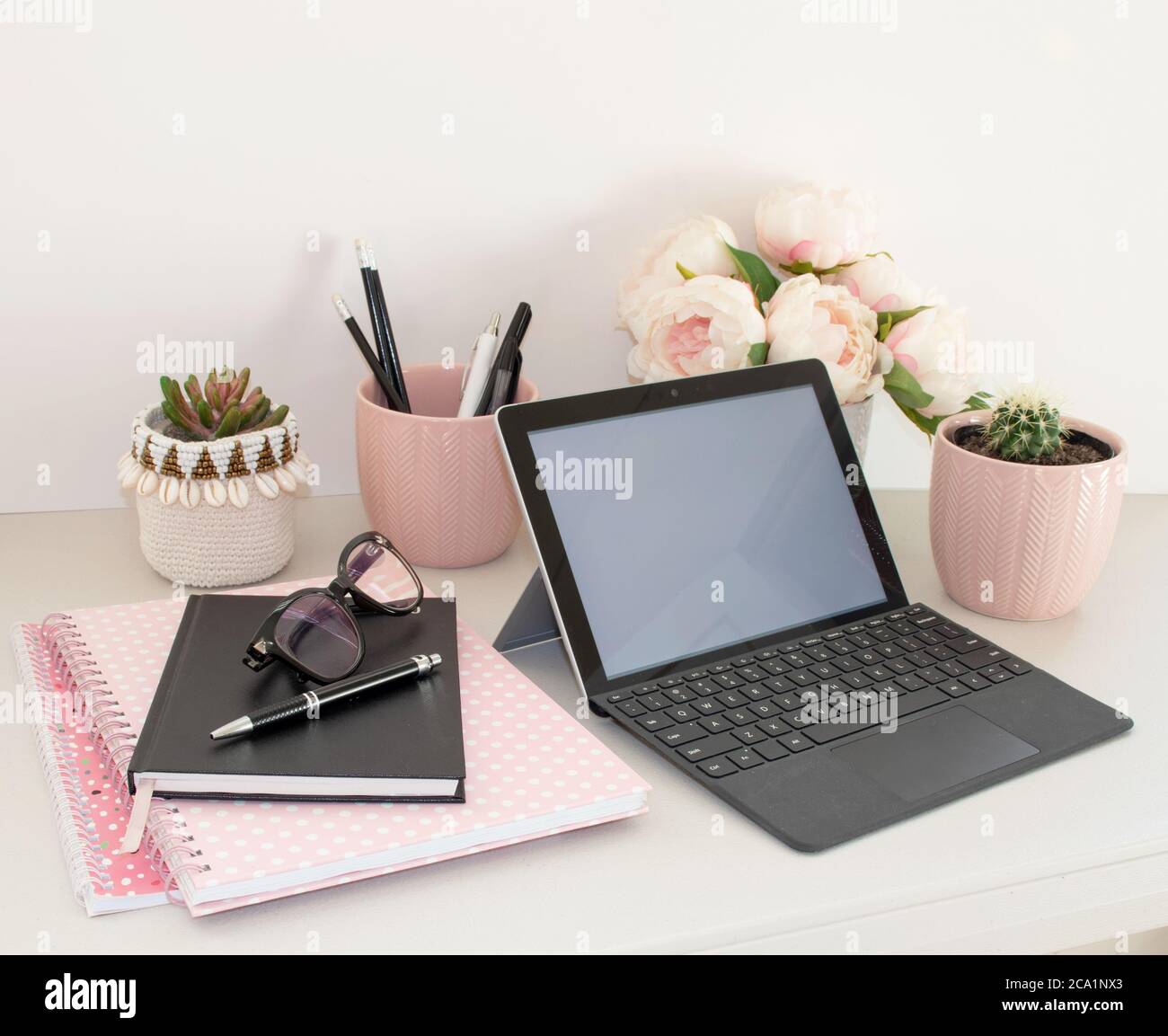 working from home office laptop with pink notebooks and flowers and potted plants Stock Photo