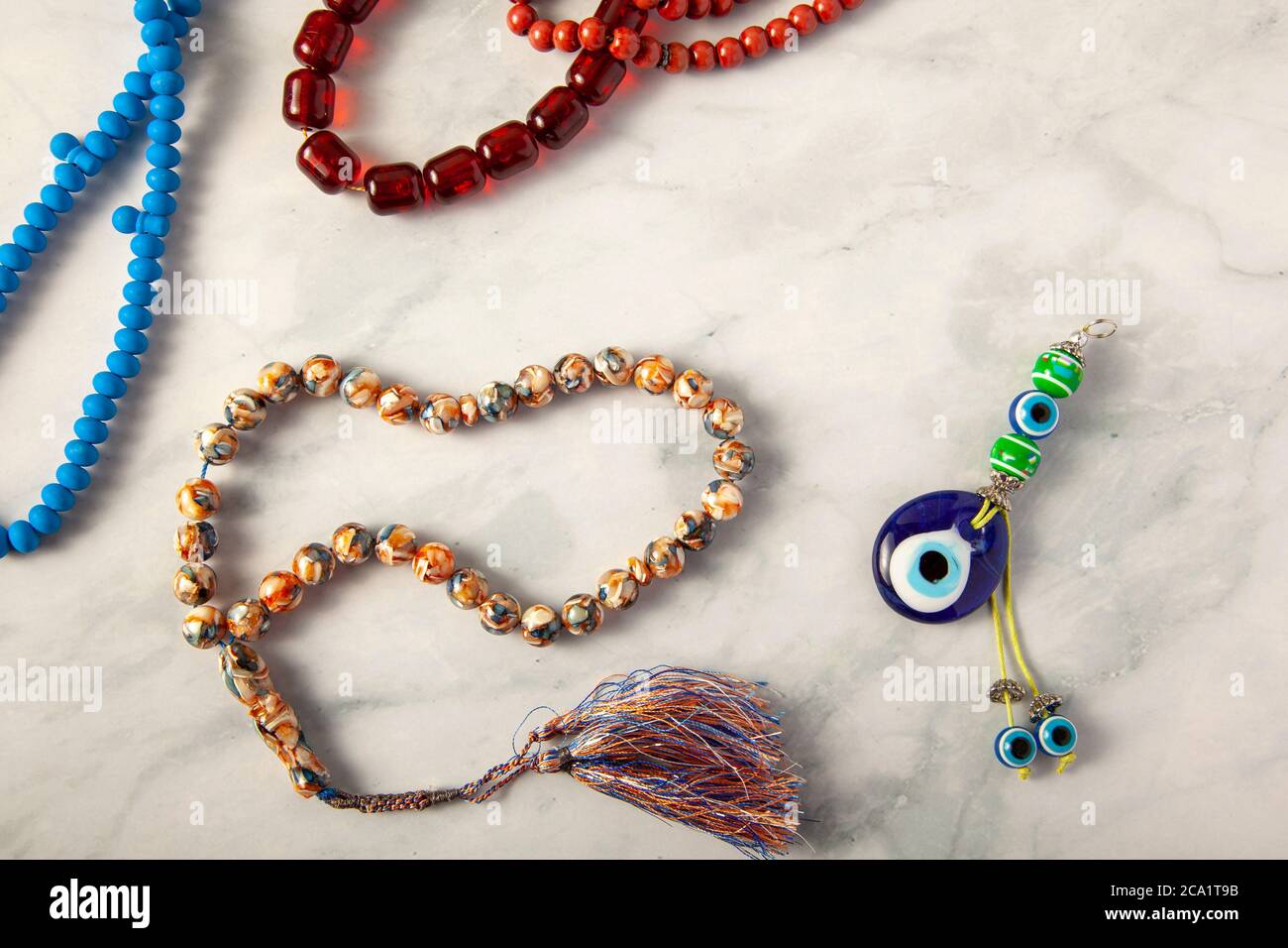 A random collection of a variety of prayer beads (tesbih) arranged on marble background. There is an evil eye amulet in the middle that according to T Stock Photo