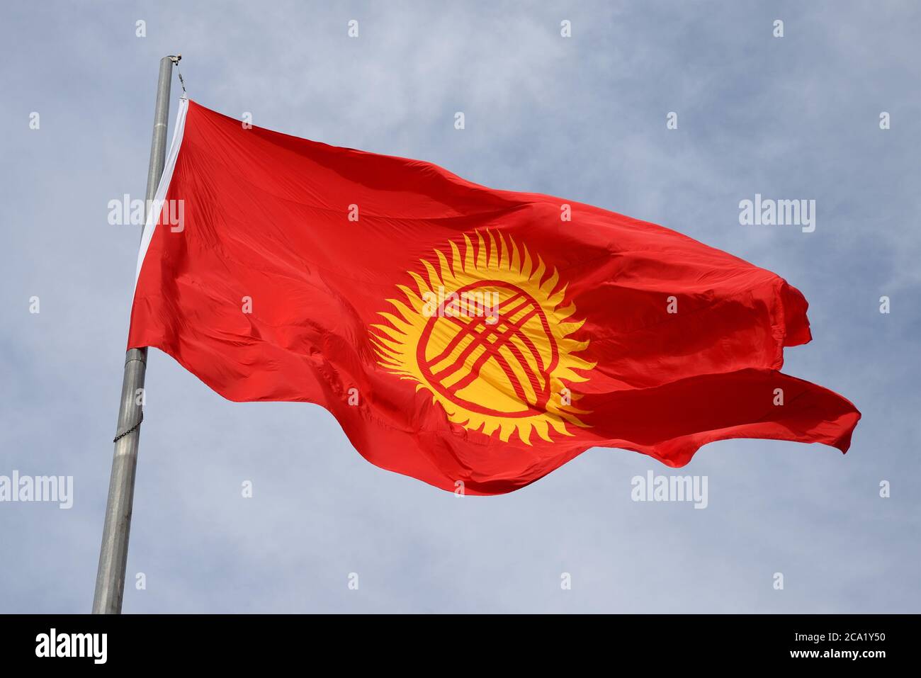 Kyrgyzstan flag waving at a pole in Bishkek. Red flag with yellow tunduk in front of sky. Stock Photo