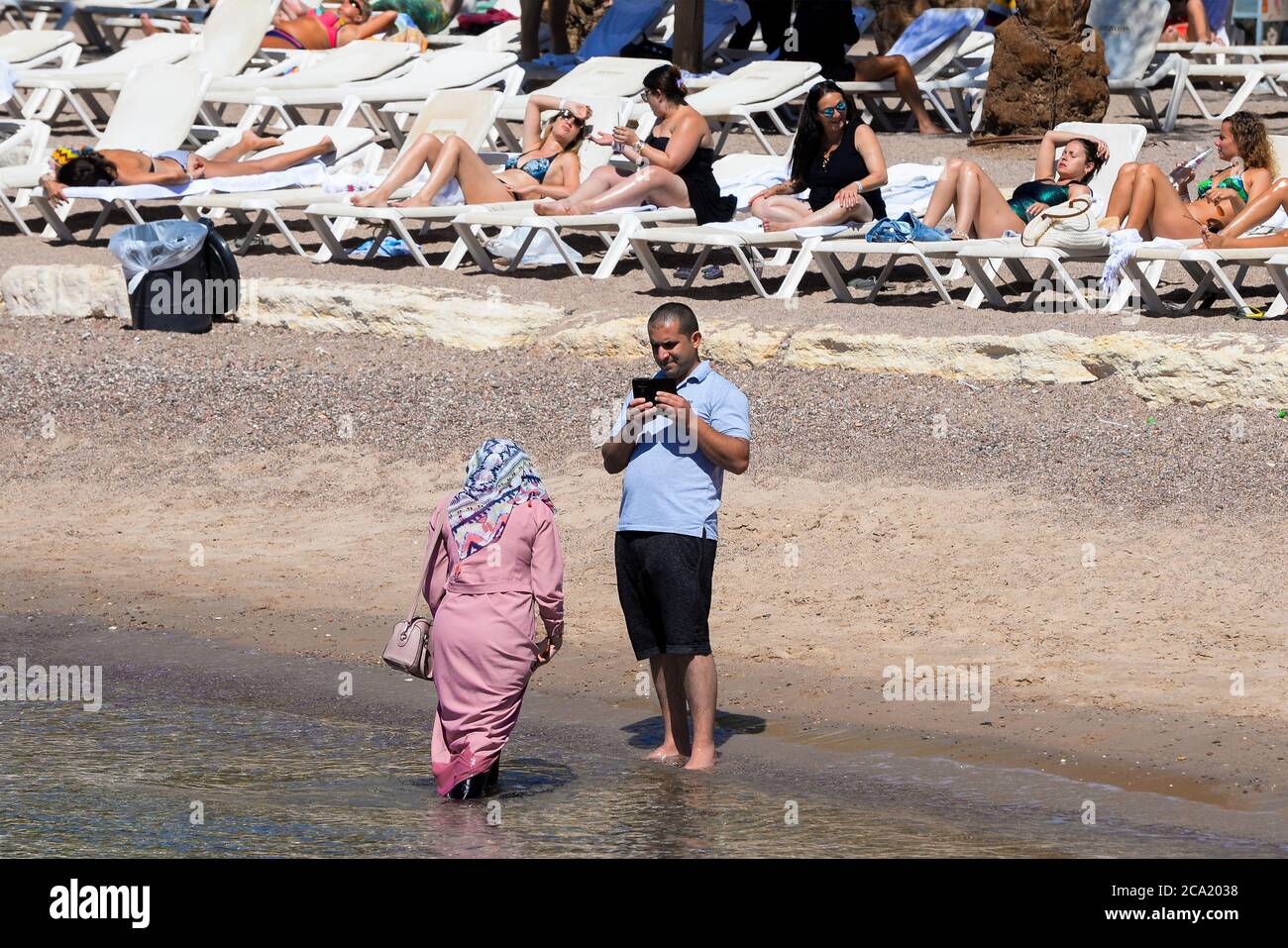 Muslim woman covered with hijab on the sea while other women sunbathe