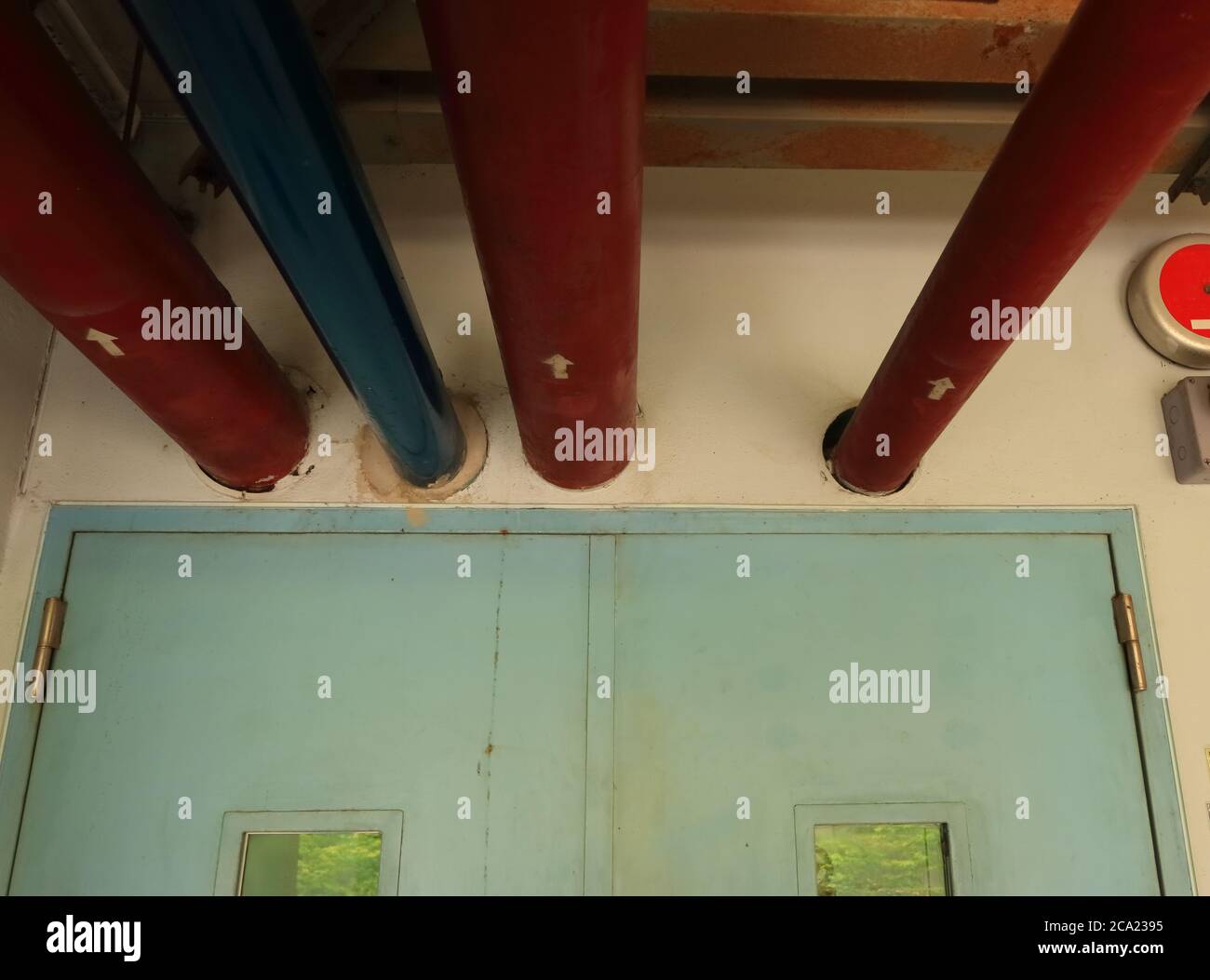 Selective focus on part of water pipes installed above closed door and run through the wall into pump room, the red pipes are used for fire fighting Stock Photo